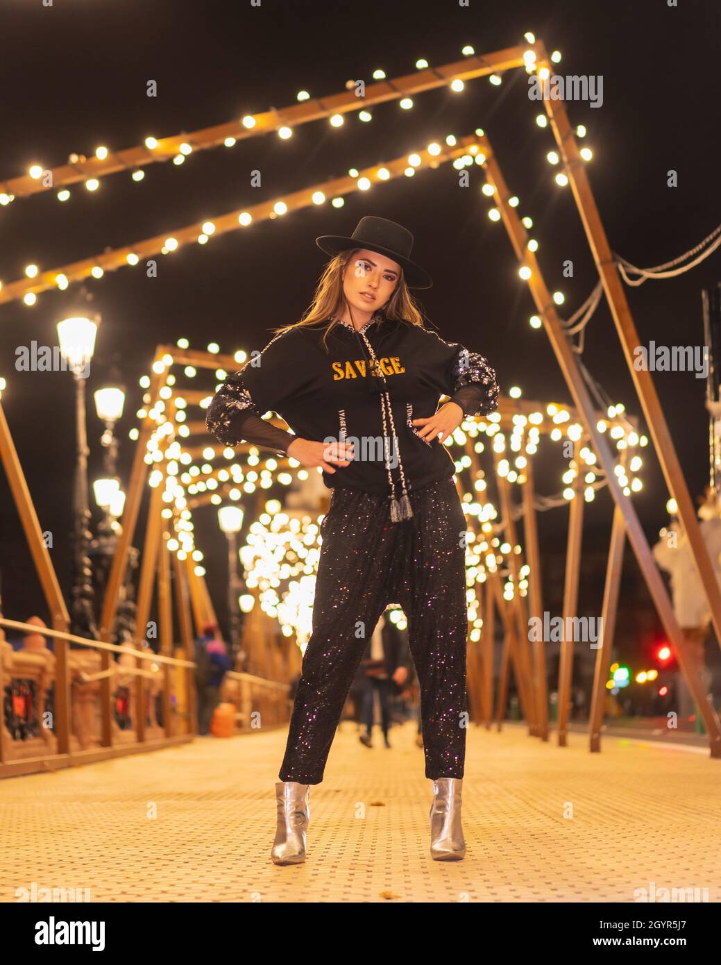 Femme blonde élégante dans un chapeau posé dans la rue illuminée la nuit dans la Christma Banque D'Images