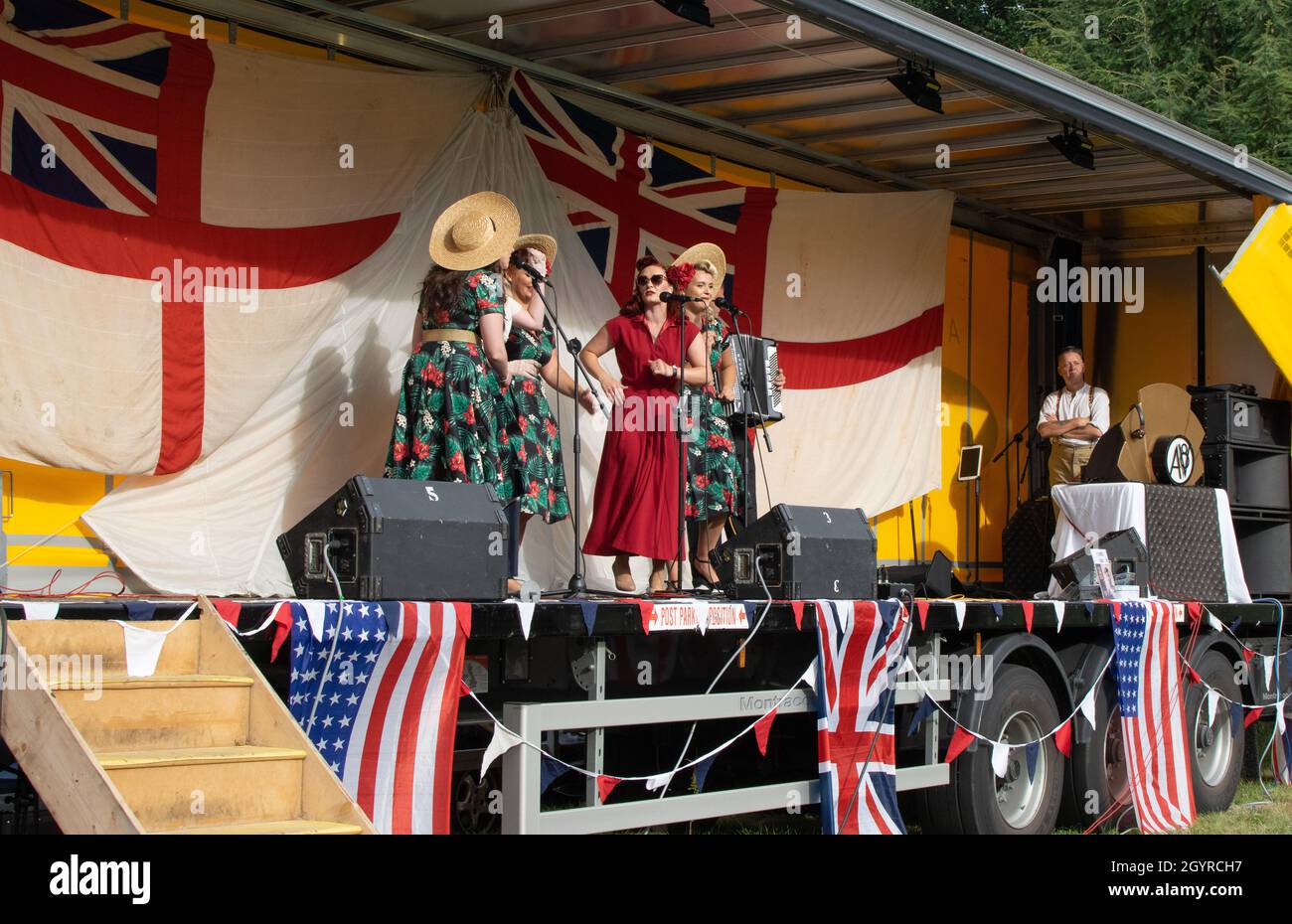 Sheringham, Norfolk, Royaume-Uni - SEPTEMBRE 14 2019 : groupe de femmes dans des vêtements des années 1940 chantant sur une scène avec des drapeaux britanniques et américains pendant le week-end des années 40 Banque D'Images