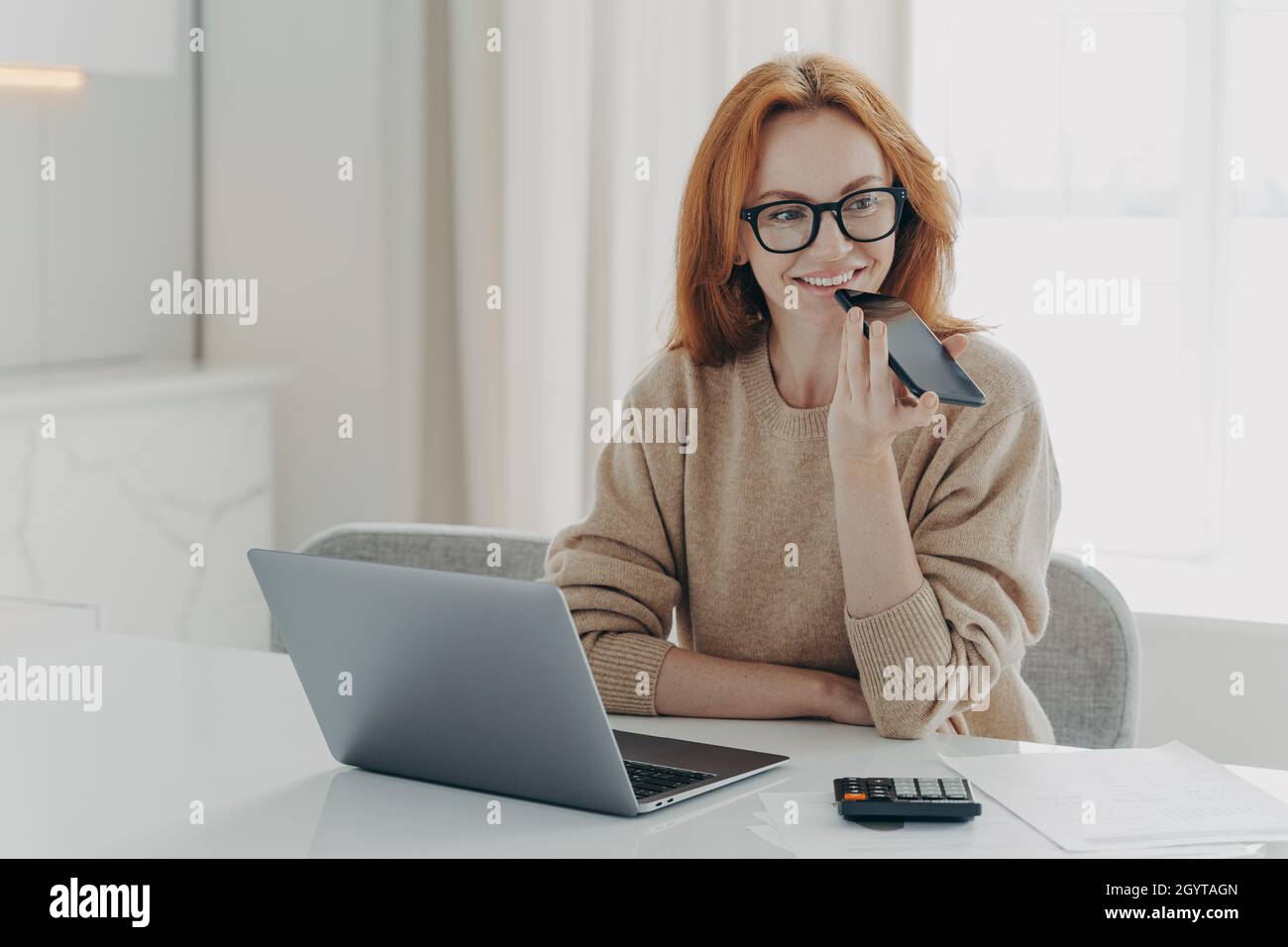 Femme souriante comptable financier utilise le système de reconnaissance vocale sur smartphone, enregistre les messages audio Banque D'Images