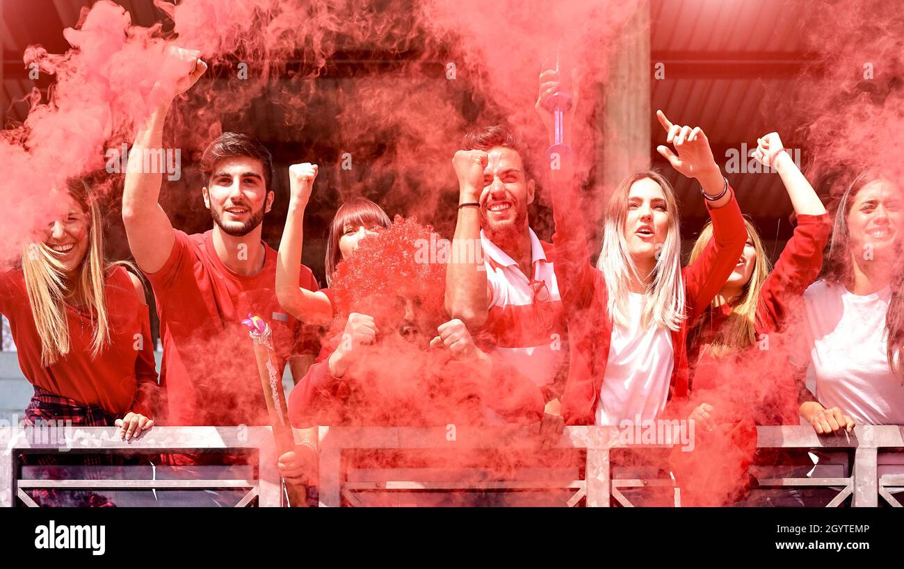 Les jeunes fans de football applaudissent avec la fumée colorée regardant le match de football ensemble au stade - amis gens de groupe avec des t-shirts rouges ayant ex Banque D'Images