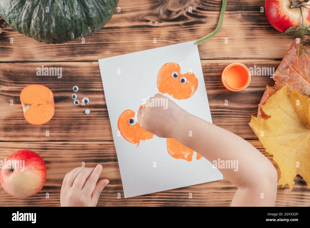 Étape par étape Halloween tutorial enfants potiron pommes imprimés.Étape 13 : la main de l'enfant goutte une goutte de colle sur l'imprimé citrouille.Vue de dessus Banque D'Images