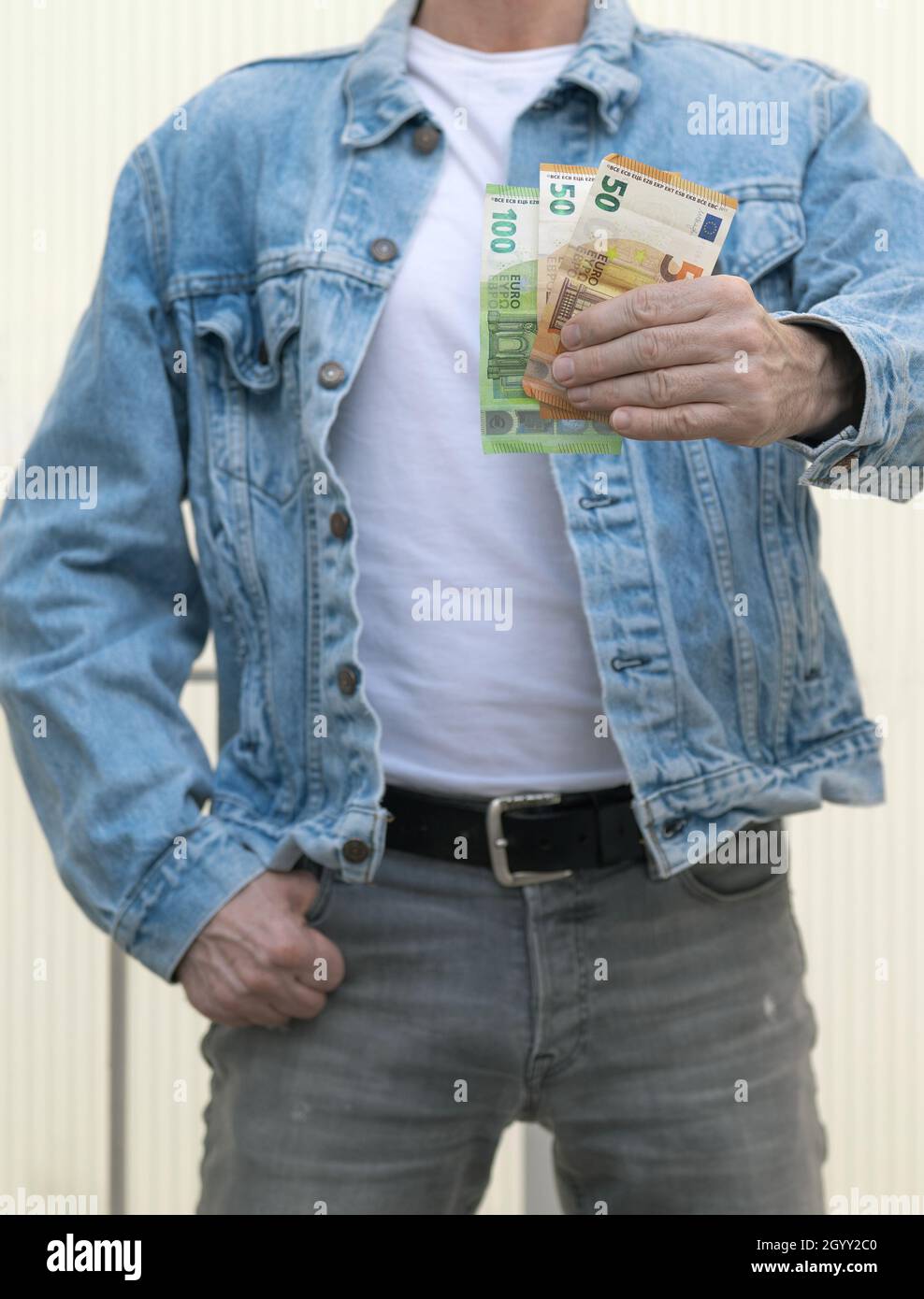 Homme en jeans gris et veste en denim bleu tient des notes d'euro dans sa main. Banque D'Images