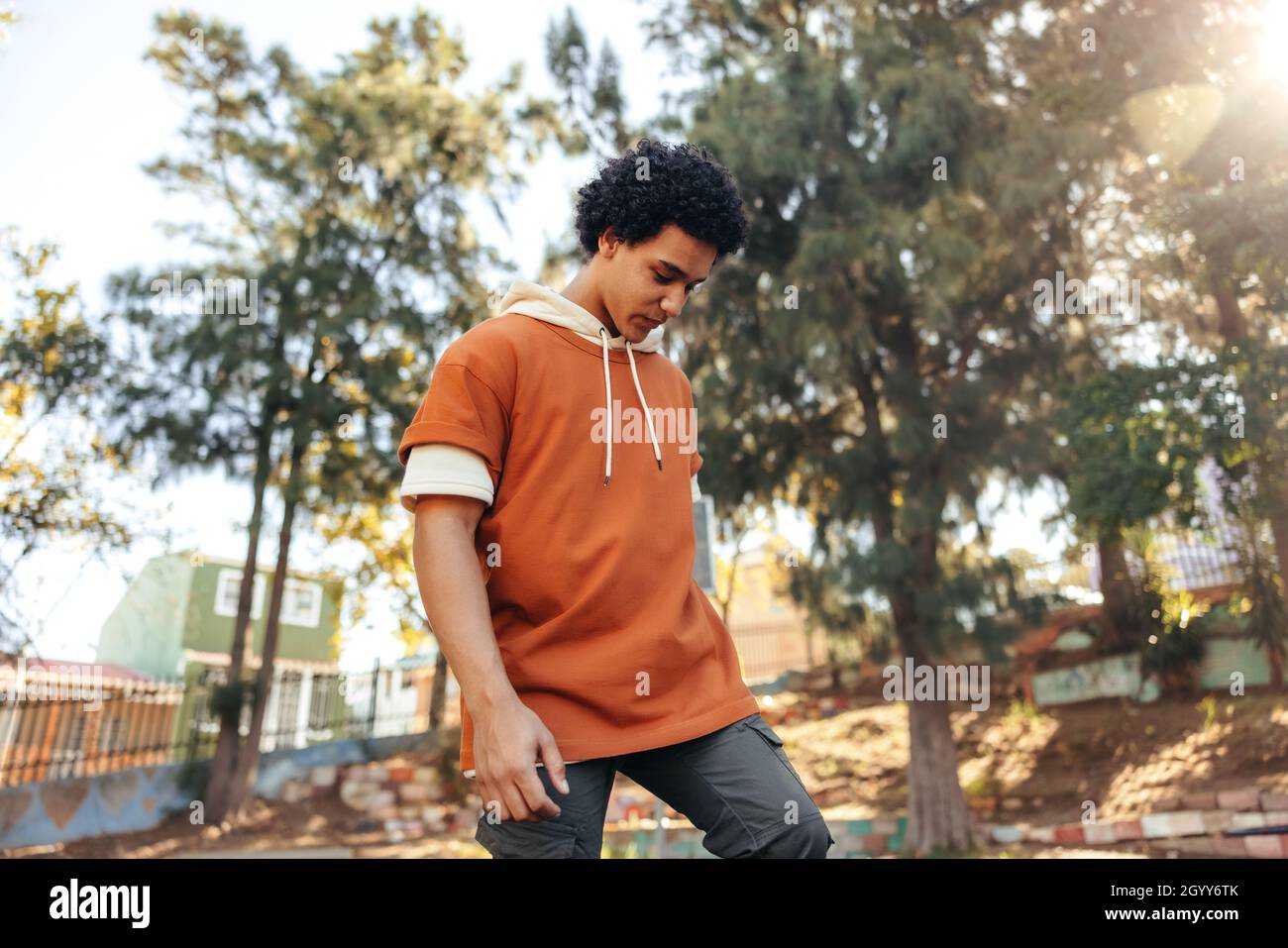 Adolescent sportif jouant avec son skateboard dans un parc urbain.Skateboarder insouciant debout seul à l'extérieur pendant la journée.Skateboard pour adolescent Banque D'Images