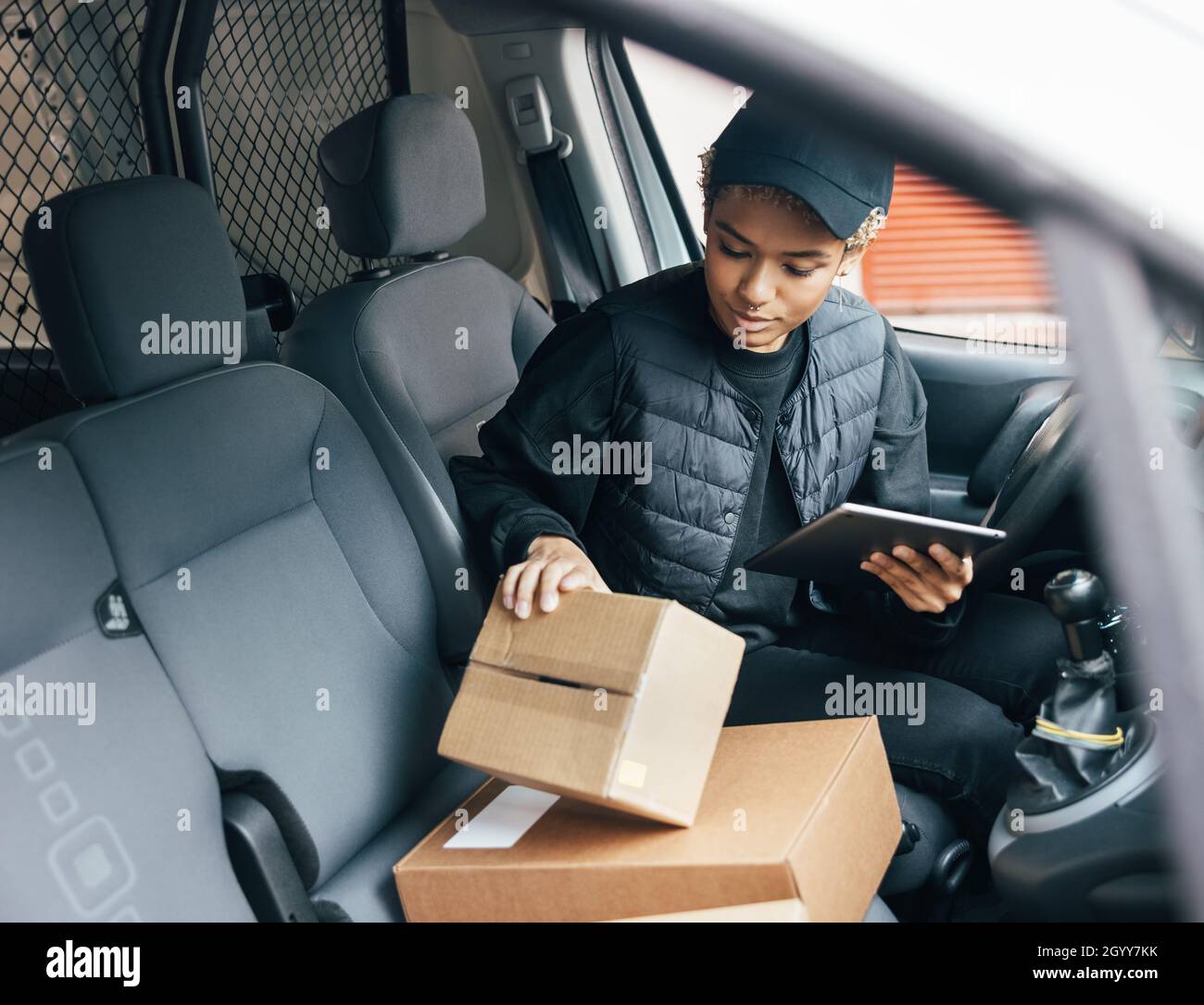 Une femme de messagerie vérifie les informations sur la boîte en carton lorsqu'elle est assise dans une voiture à l'aide d'une tablette numérique Banque D'Images