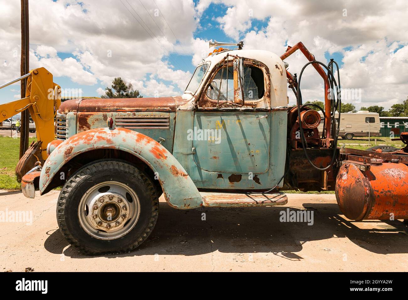 Vieux camion IH de moissonneuse international rouillé avec peinture bleue et blanche garé un jour ensoleillé à côté d'une machine industrielle dans le chantier naval Banque D'Images