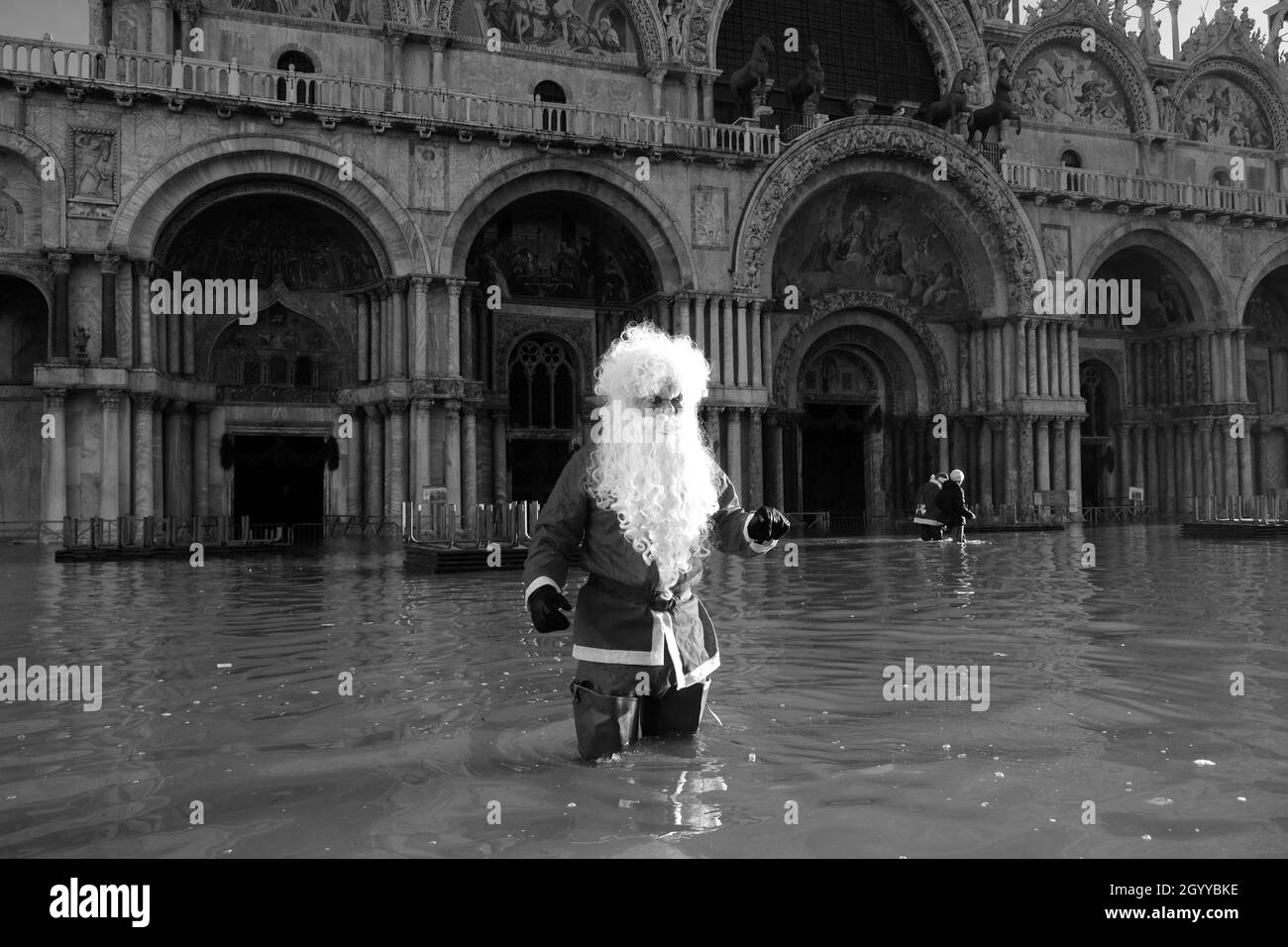 Un homme habillé comme le Père Noël traverse la place Saint-Marc pendant la marée haute à Venise, Italie, le 23 décembre 2019. Banque D'Images