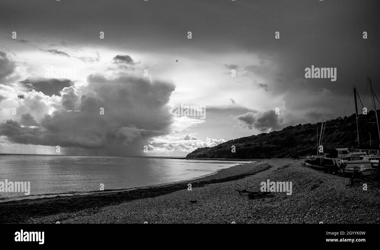 La baie de Lyme, le long de la côte jurassique, le rivage balaie autour d'un bas nuage dramatique à l'horizon, les bateaux sur shingle dans le premier plan droit Banque D'Images