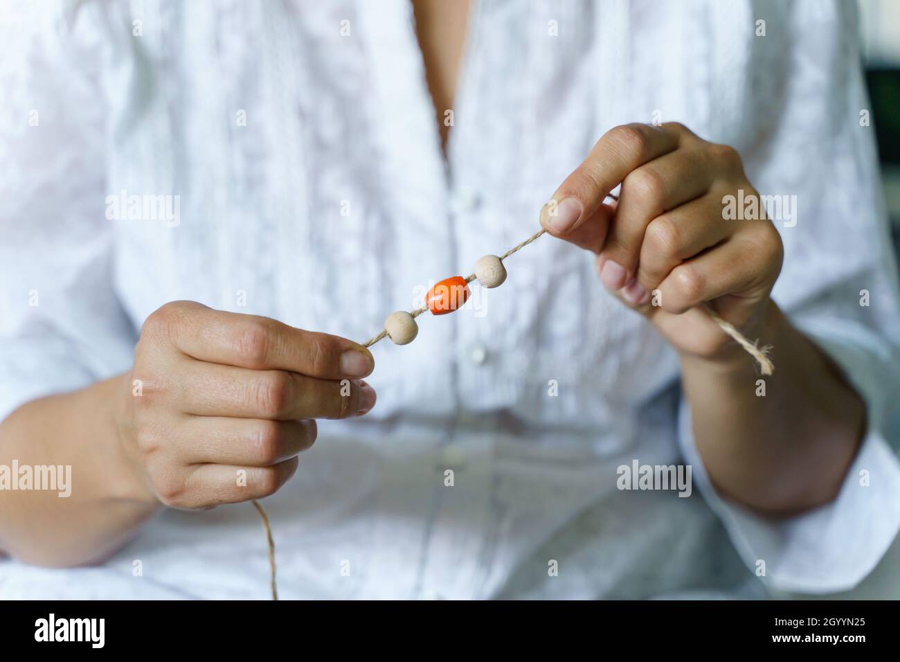 Gros plan sur la section médiane d'une femme inconnue tenant une ficelle avec des perles en bois ou en plastique faisant des matériaux nature bracelet collier à la maison - Creative des Banque D'Images