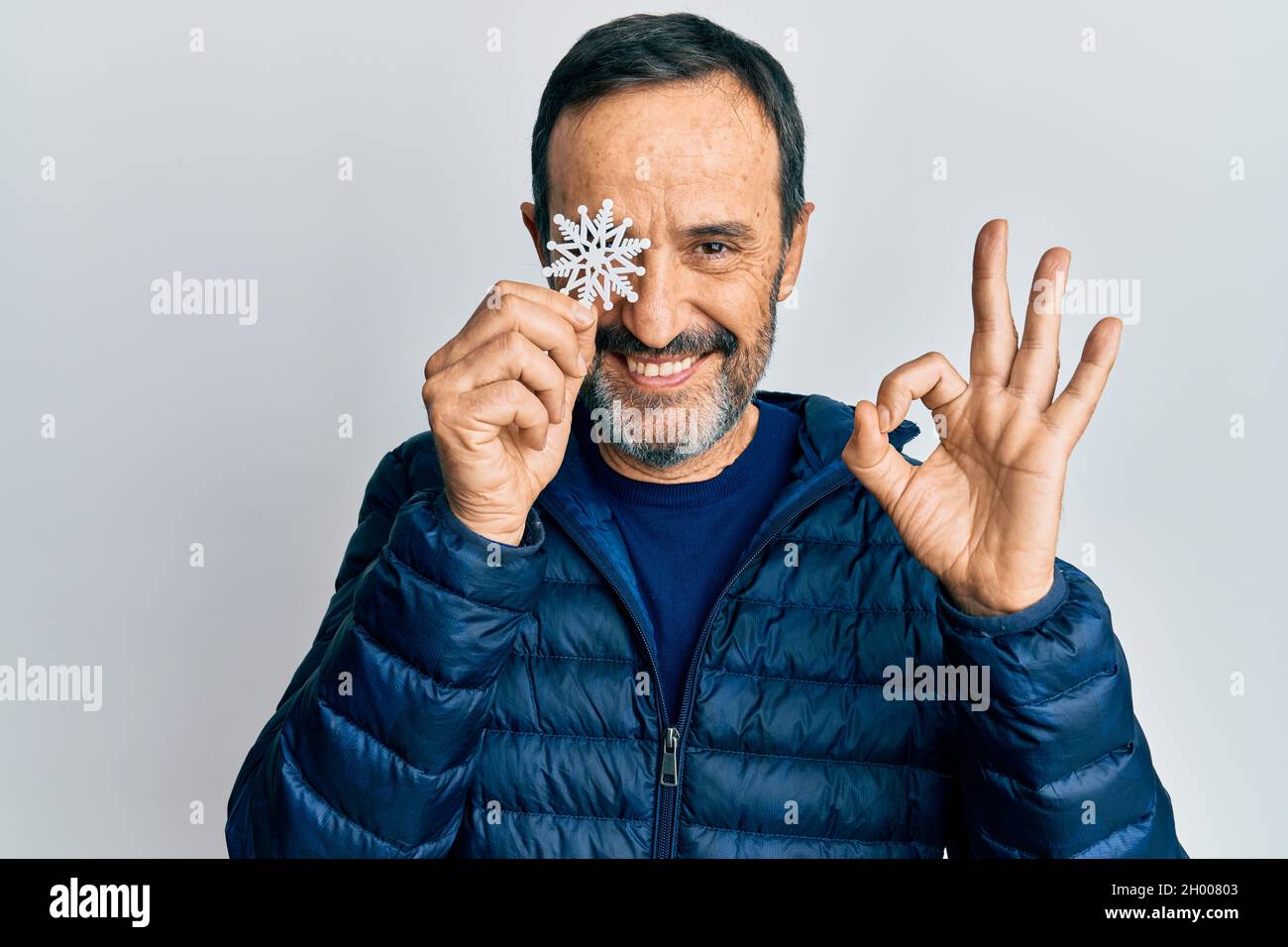 Homme hispanique d'âge moyen tenant un flocon de neige sur l'œil faisant signe ok avec les doigts, souriant sympathique gesturant excellent symbole Banque D'Images
