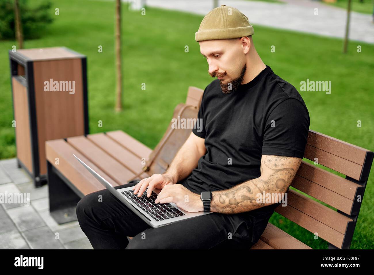 Un homme barbu sérieux s'assoit à l'extérieur tout en tapant du texte sur un ordinateur portable.Connexion Internet 4G Banque D'Images