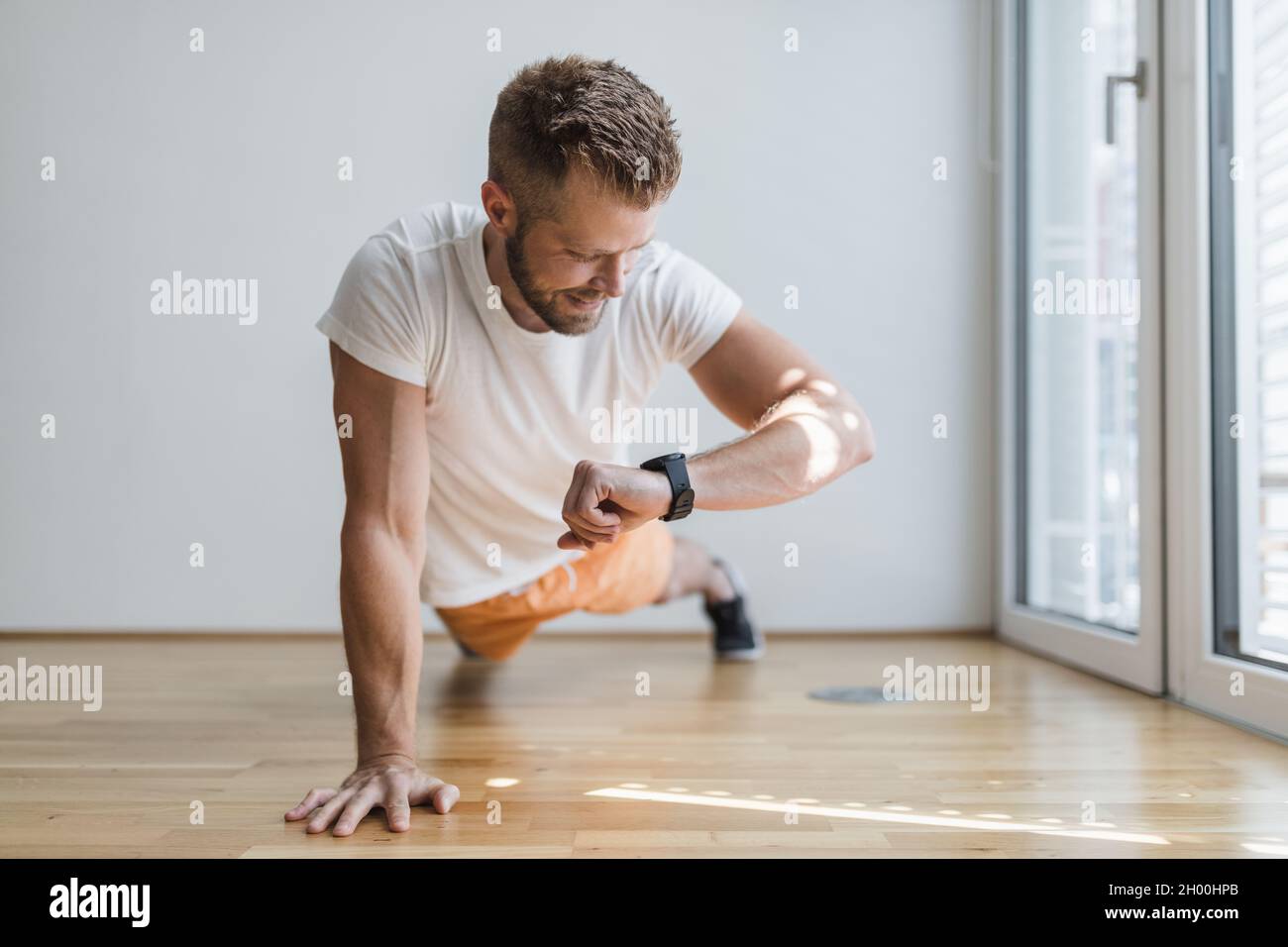 Beau jeune homme qui fait de l'activité à la maison avec un intelligent regardez Banque D'Images