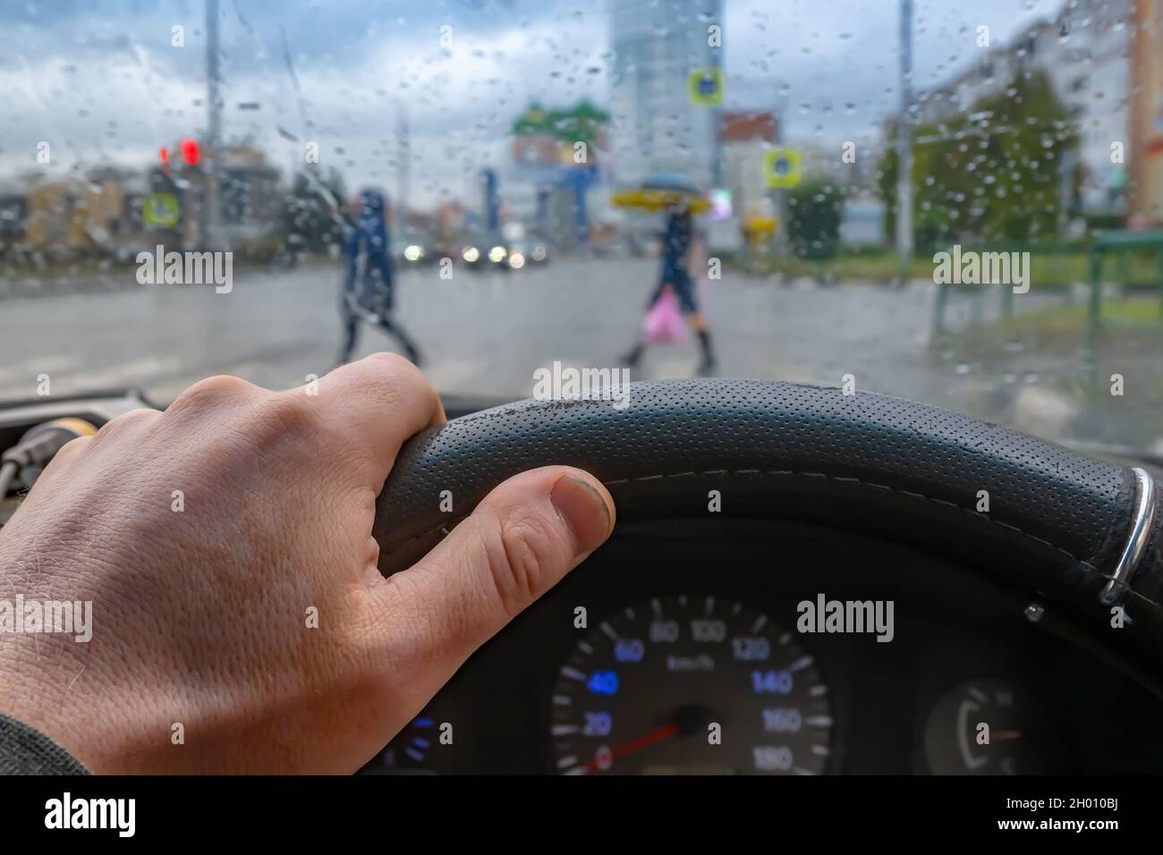 vue de la main du conducteur sur le volant de la voiture sur le fond de l'intersection sous la pluie Banque D'Images