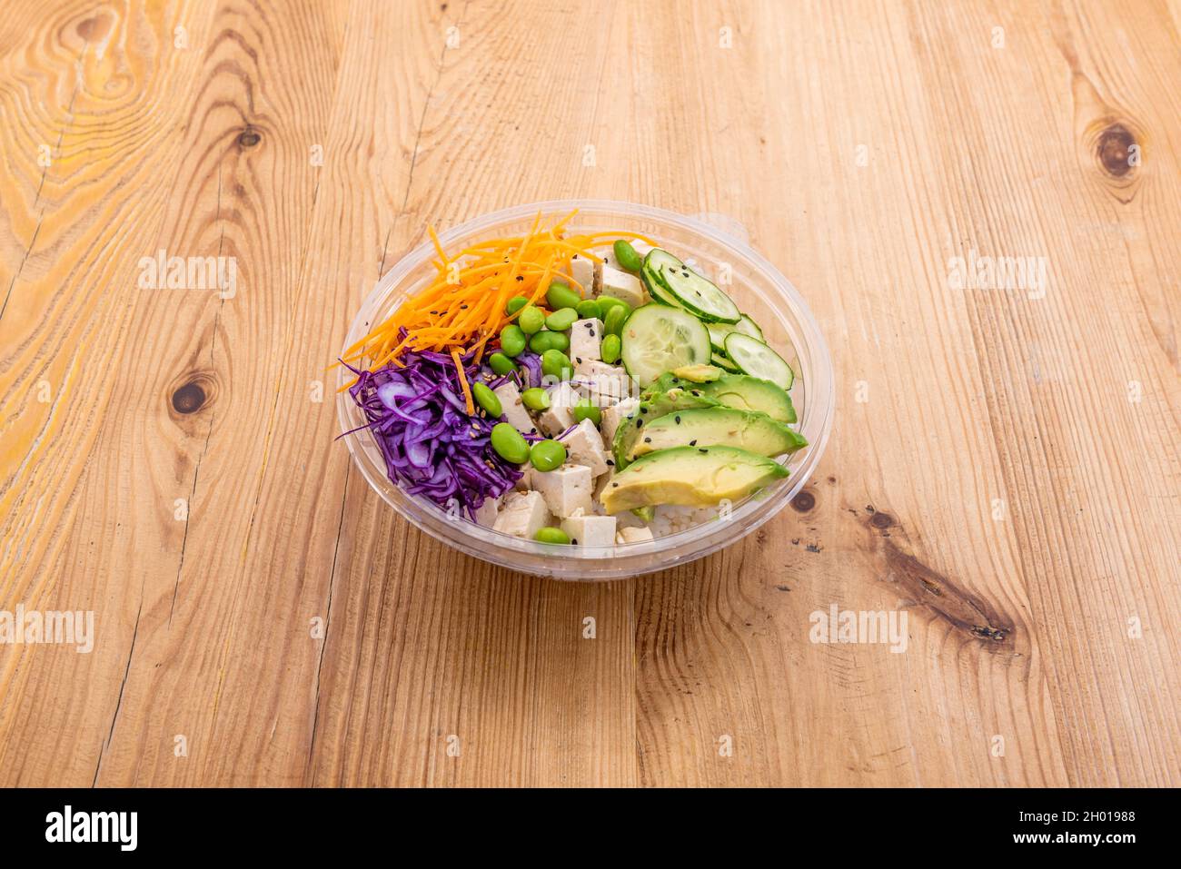 Bol végétalien avec taco tofu, riz blanc, morceaux d'avocat mûrs, haricots édamames, chou rouge et carottes râpées dans un récipient à emporter Banque D'Images