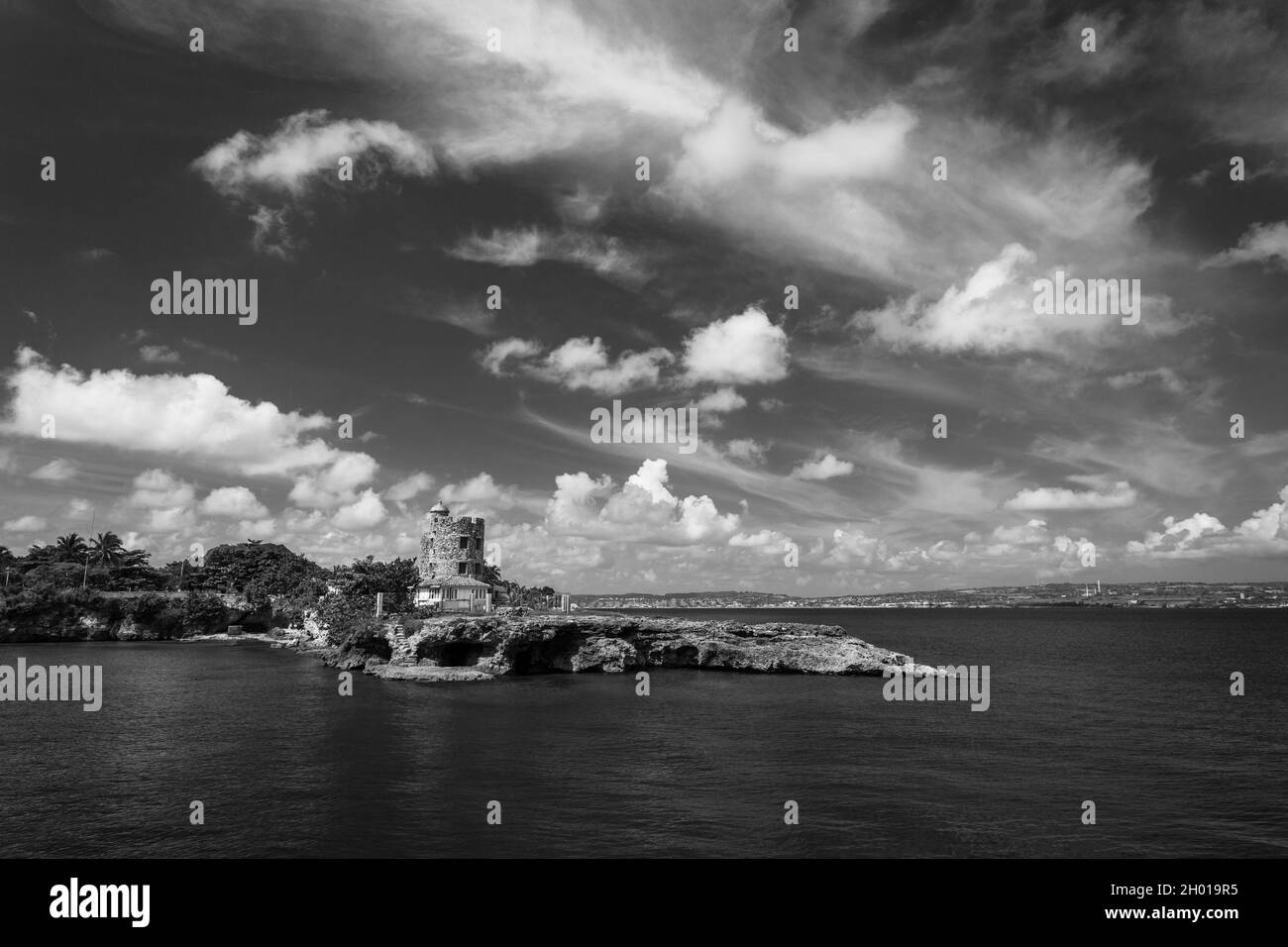 Vue tropicale de la région côtière avec une tour et des plages avec eau turquoise calme, ciel nuageux et bleu, rochers en premier plan et quelques arr de verdure Banque D'Images