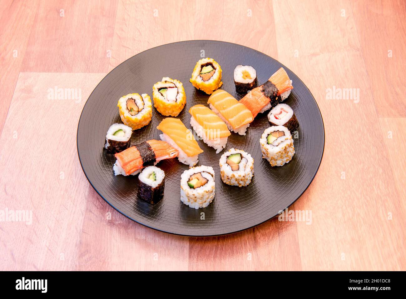 Assiette ronde noire avec mélange de sushi, maki avec concombre, nigiri de saumon norvégien et surimi, riz blanc avec vinaigre japonais, rouleau de californie uramaki Banque D'Images