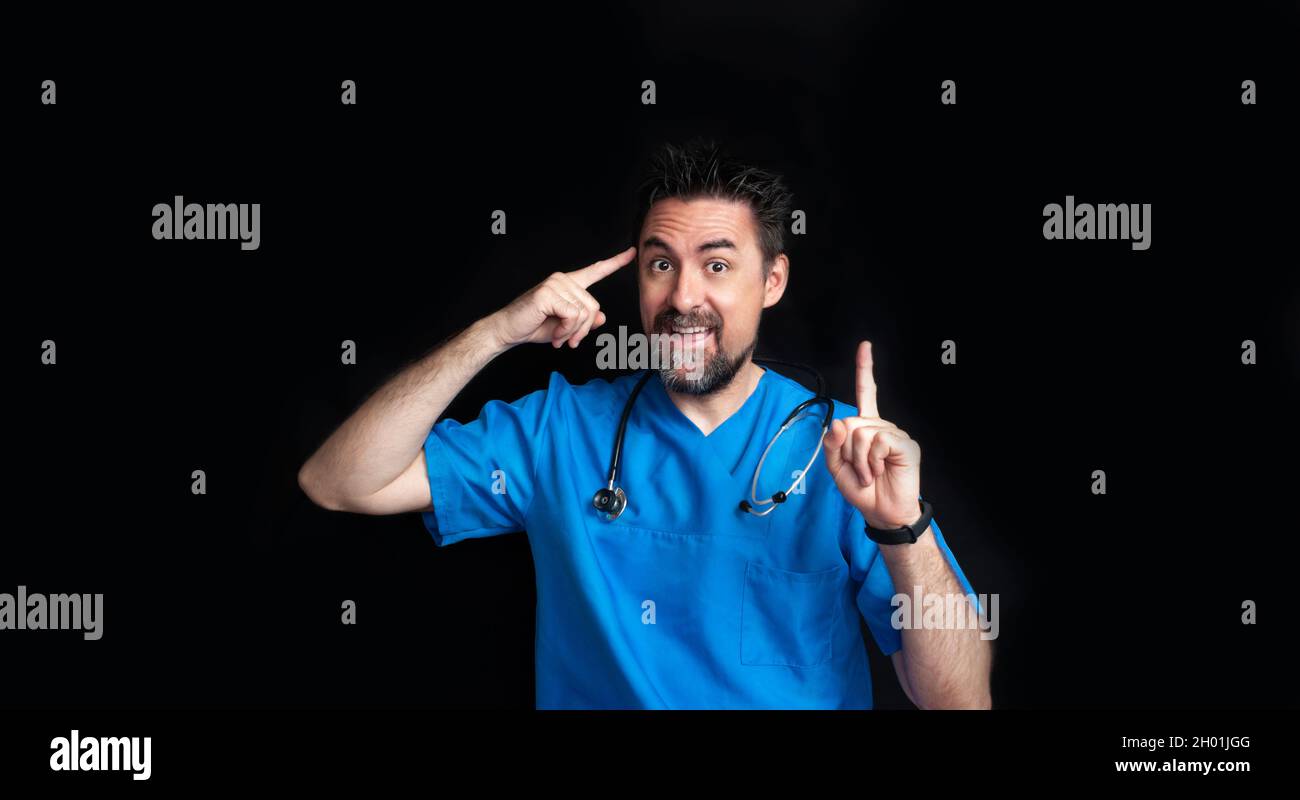 Un médecin dans un uniforme d'hôpital bleu avec un stéthoscope autour de son cou, levant ses sourcils et pointant un doigt vers sa tête et en levant un indice fi Banque D'Images