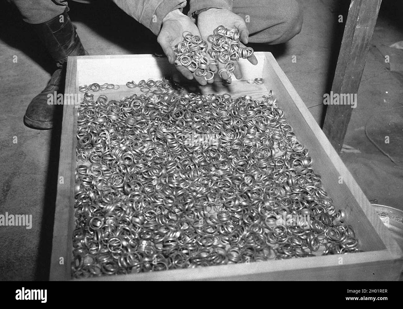 Un soldat américain inspecte des milliers d'anneaux de mariage en or pris par les Juifs par les Allemands et écrasé dans les mines de sel de Heilbronn, le 3 mai 1945 en Allemagne. Banque D'Images
