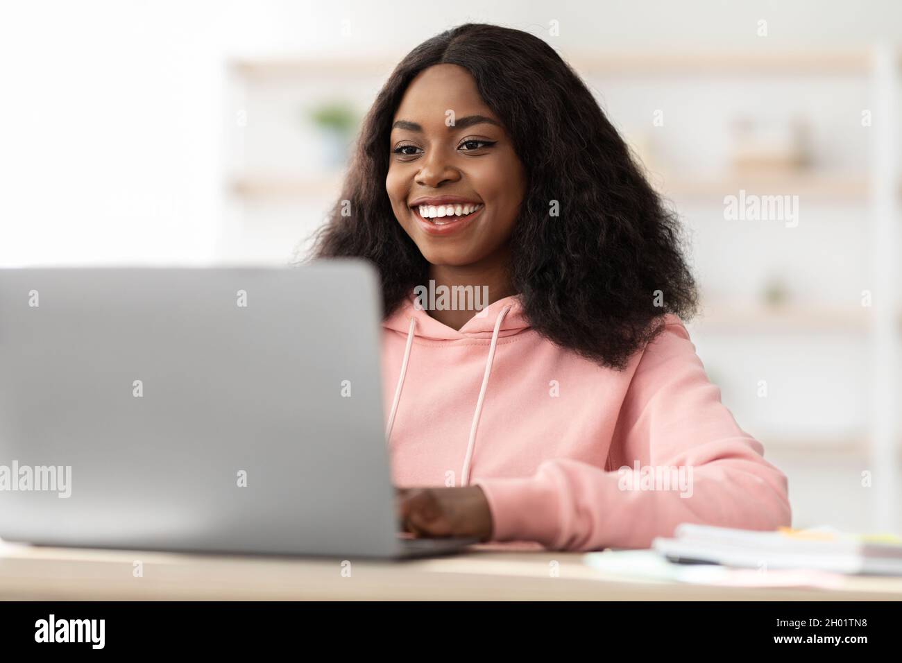 Gros plan de la jeune femme noire tapant sur le clavier de l'ordinateur portable et souriant, envoyant des e-mails aux clients, intérieur de bureau.Jolie dame afro-américaine Banque D'Images