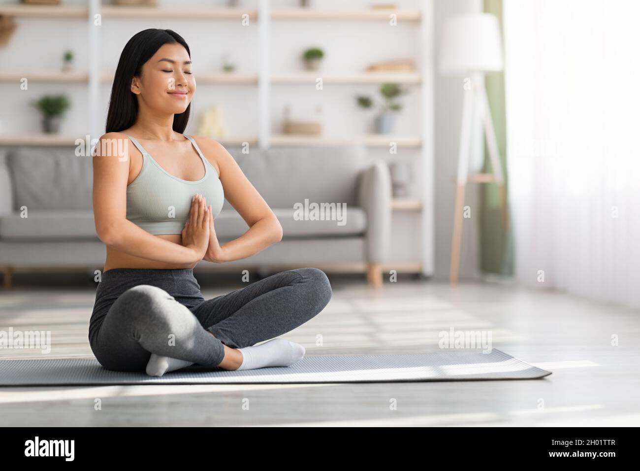 Yoga du matin.Portrait d'une jeune femme asiatique calme méditant à la maison, femme coréenne détendue assise en position lotus avec les yeux fermés et la main clasdée Banque D'Images