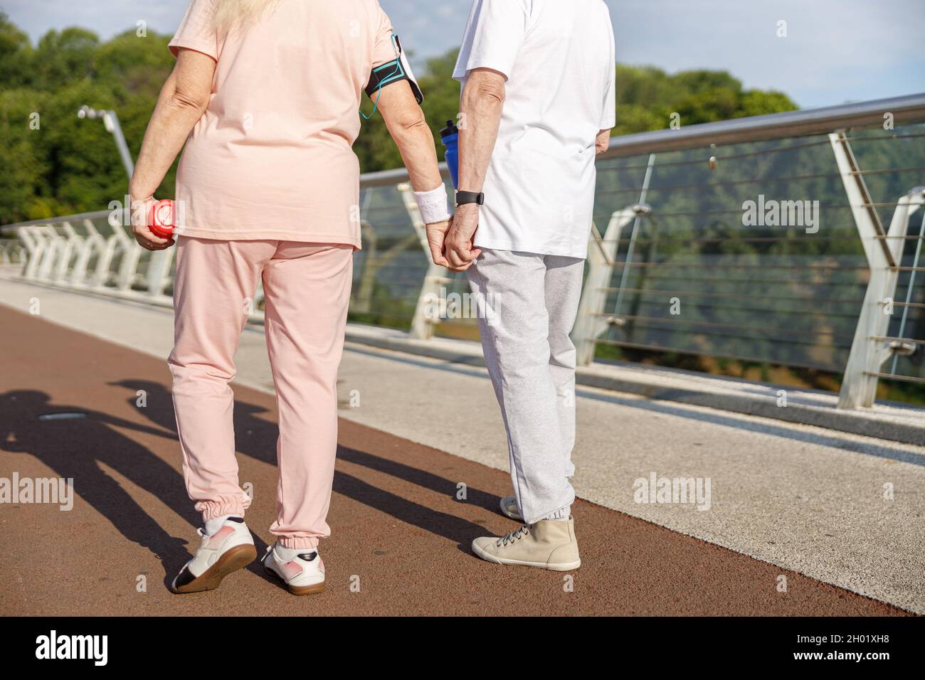Un couple senior en survêtements se joindra aux mains le long de la passerelle au coucher du soleil Banque D'Images