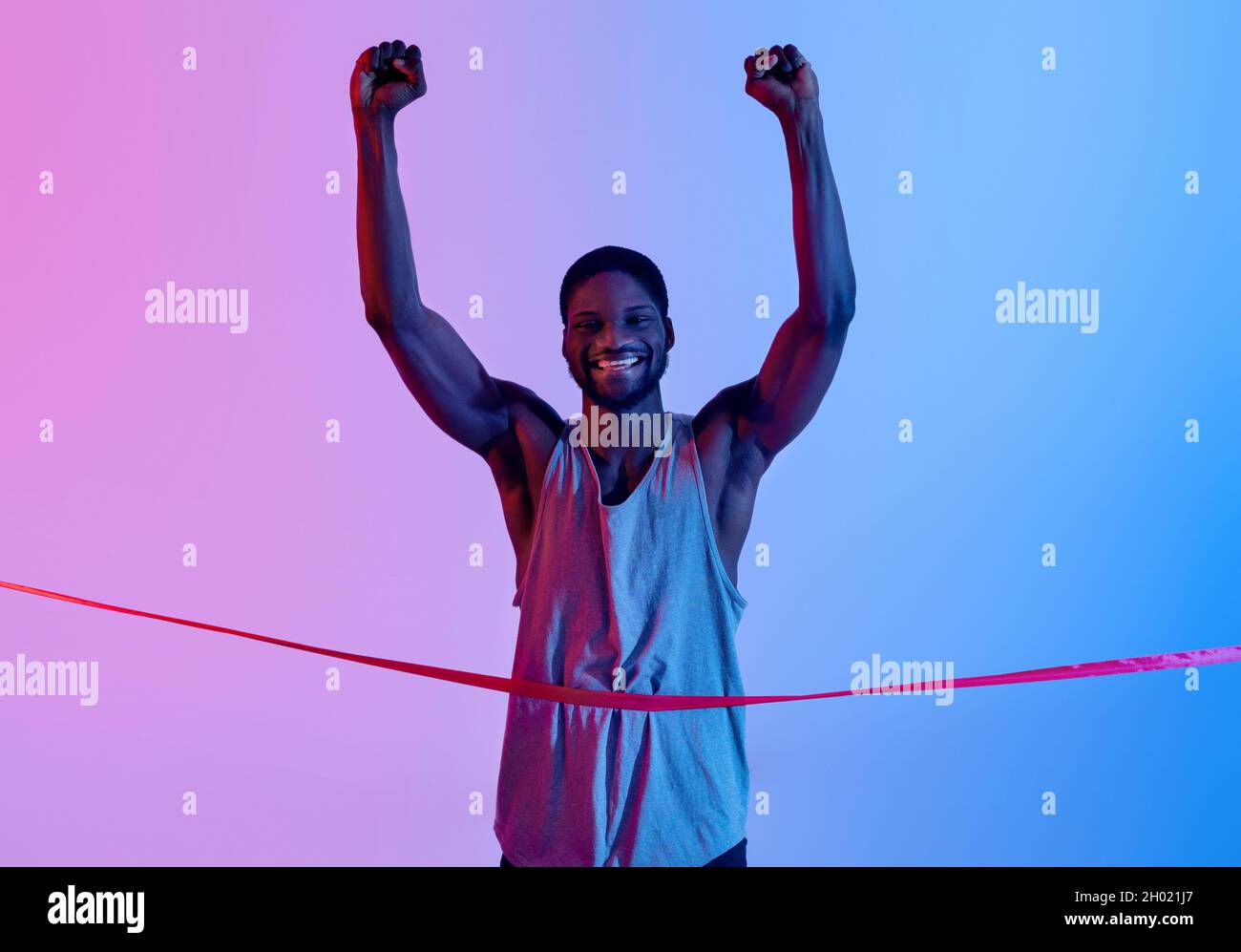 Un sportif noir enthousiaste qui s'exécute, franchit la ligne d'arrivée, élève ses bras en triomphe et célèbre la victoire dans l'éclairage au néon.Une Amérique africaine émotionnelle Banque D'Images