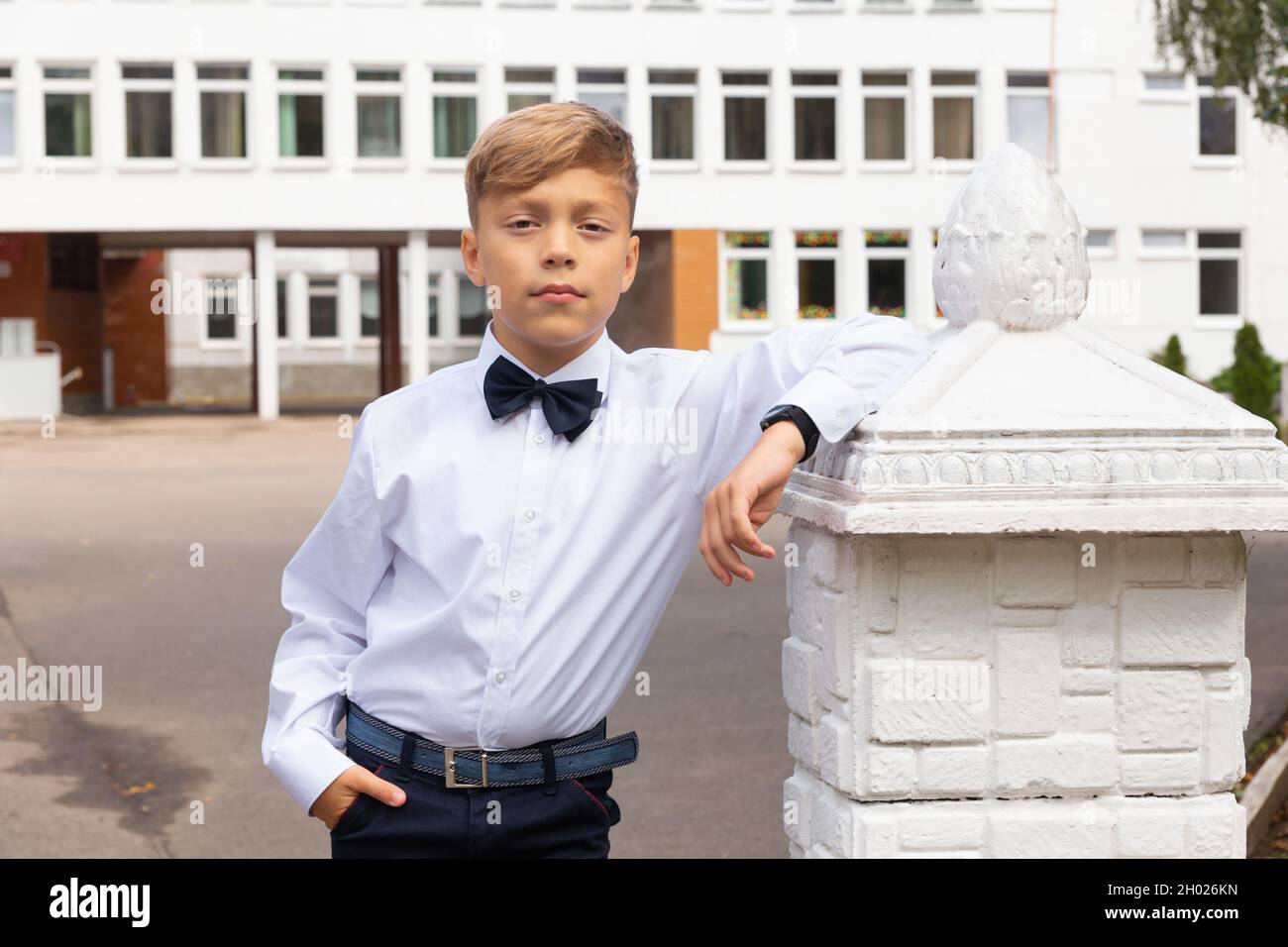 Un beau garçon de huit ans dans un uniforme d'école, un pantalon noir et  une chemise blanche avec noeud papillon pose dans la cour d'école Photo  Stock - Alamy