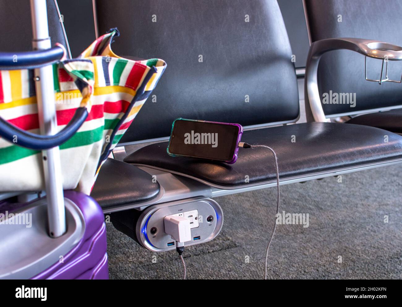 Un passager d'un aéroport utilise un plug-in prêt à l'emploi situé sous les sièges dans la zone d'attente de la porte Banque D'Images