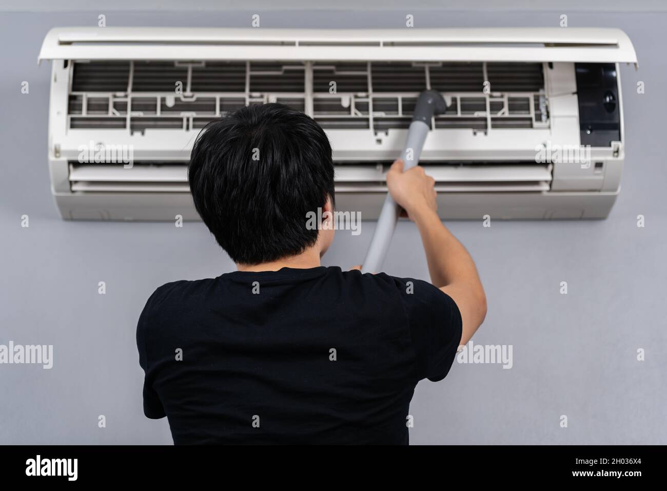 jeune homme utilisant un aspirateur pour nettoyer le climatiseur à la maison Banque D'Images