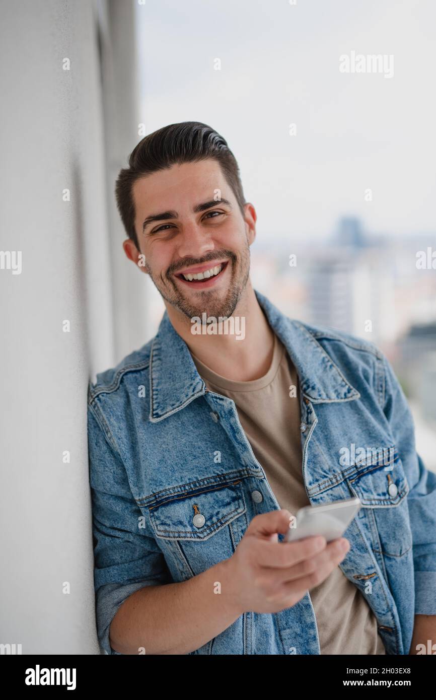 Portrait d'un jeune homme du caucase avec un smartphone debout sur un balcon, regardant l'appareil photo. Banque D'Images