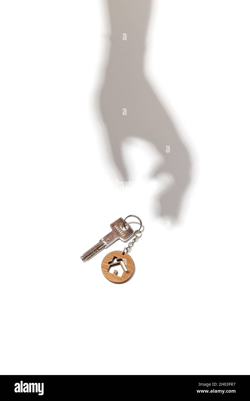 Concept immobilier.Clés avec porte-clés en forme de maison avec ombre à la main sur fond blanc. Banque D'Images