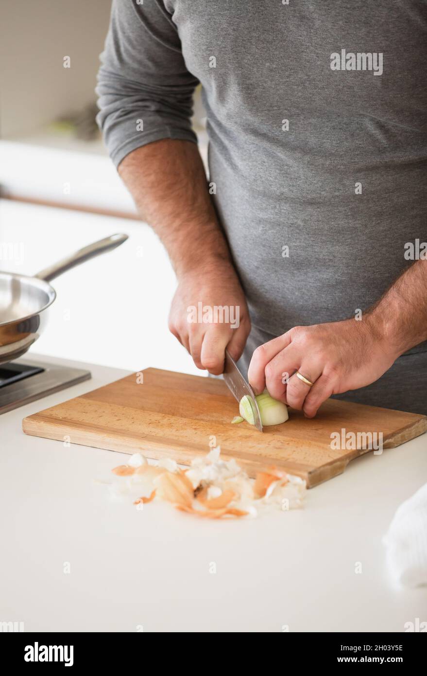 Gros plan de l'homme coupant l'oignon sur une planche en bois dans la cuisine maison Banque D'Images