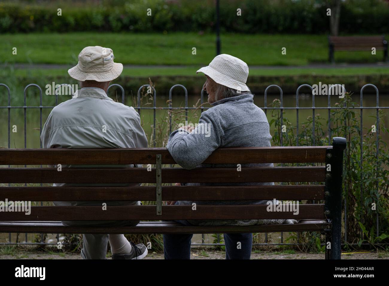 Deux amis mâles âgés portant des chapeaux de soleil et assis sur un banc pour discuter. Banque D'Images