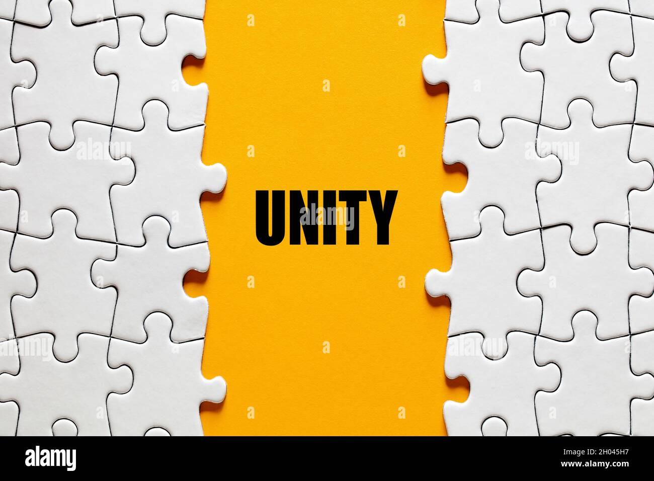 Le mot unité sur fond jaune entre les pièces du puzzle.Concept de synergie, de fusion, d'association ou d'intégration. Banque D'Images