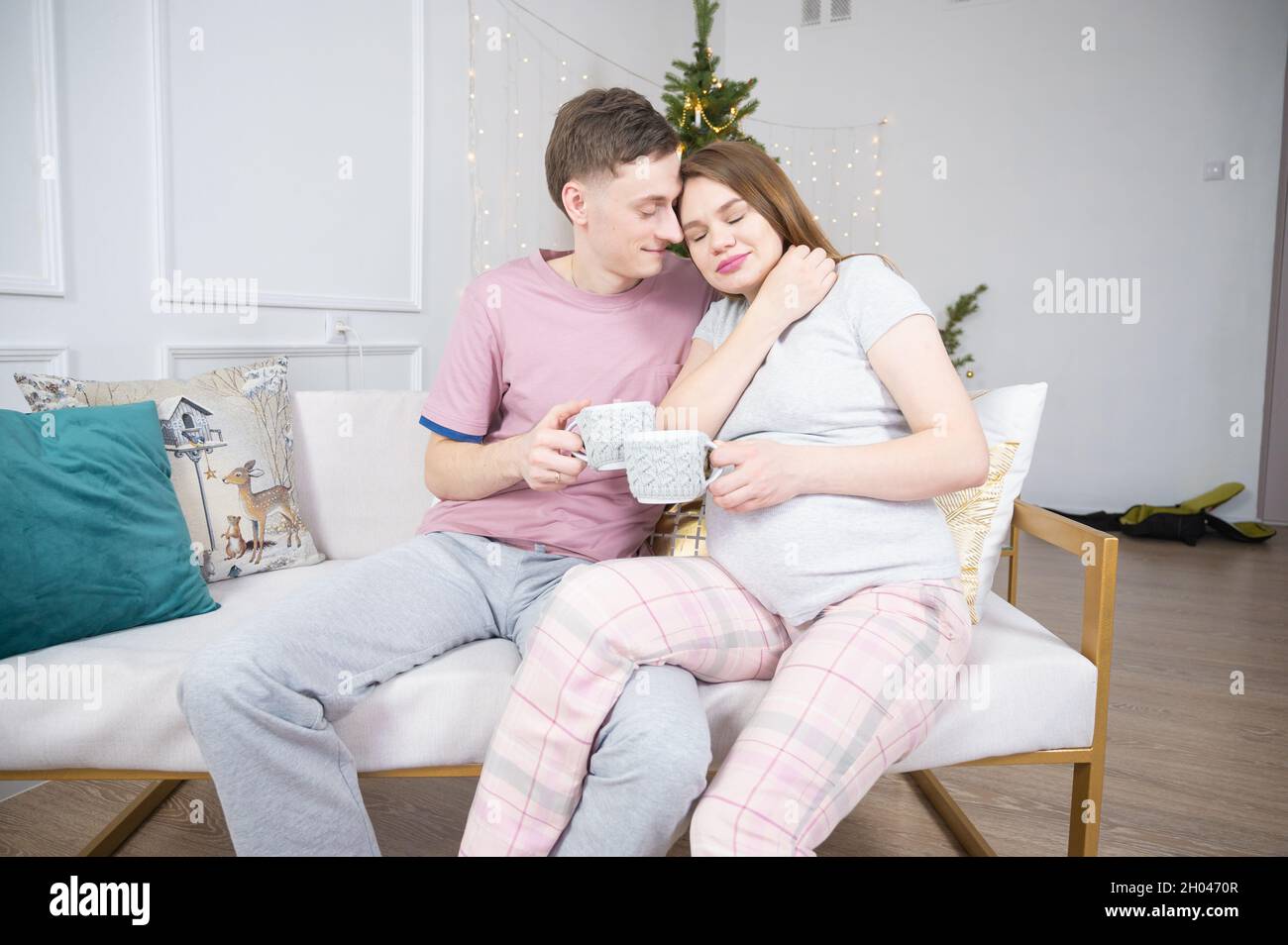 Mari prenant soin de sa femme enceinte, embrassant et embrassant. Un jeune couple se détende sur un canapé à l'heure de Noël Banque D'Images