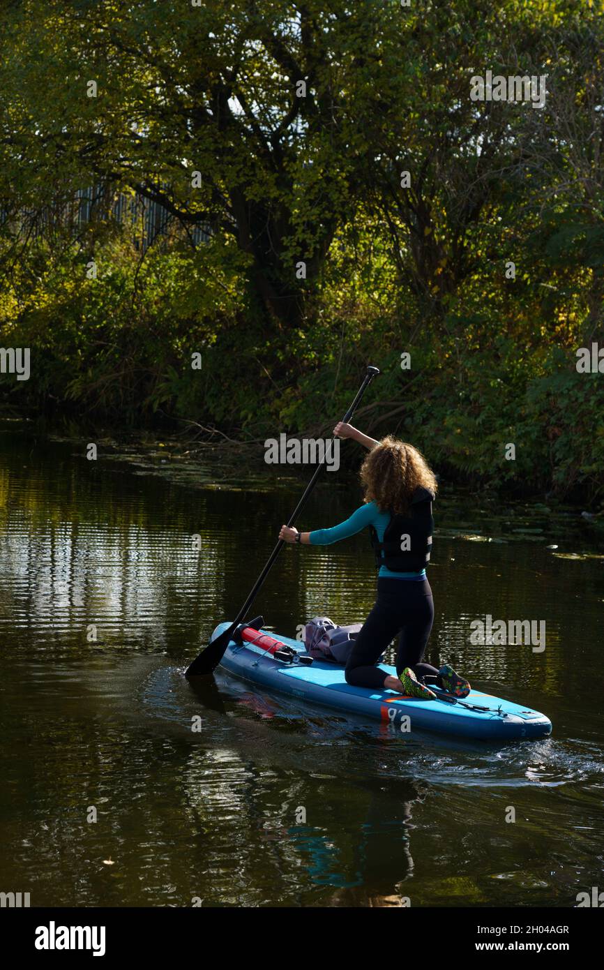 Lors d'une belle journée d'automne, une femme s'agenouille sur son paddleboard et descend le canal de Leeds et Liverpool, Leeds, West Yorkshire, Angleterre, Royaume-Uni. Banque D'Images