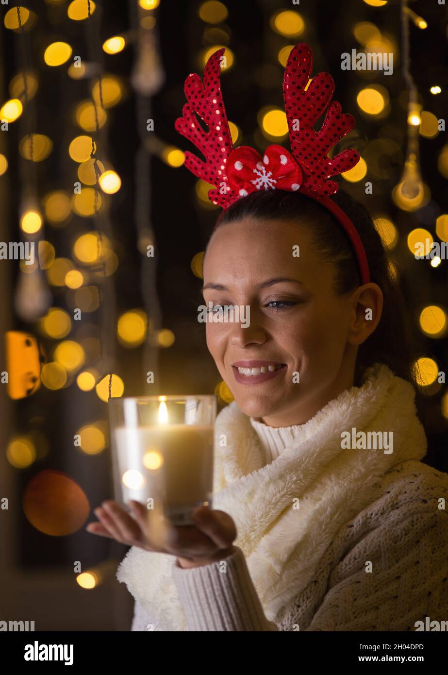 Jolie jeune fille avec des bois rouges sur la tête tenant la bougie dans la température ambiante de noël Banque D'Images