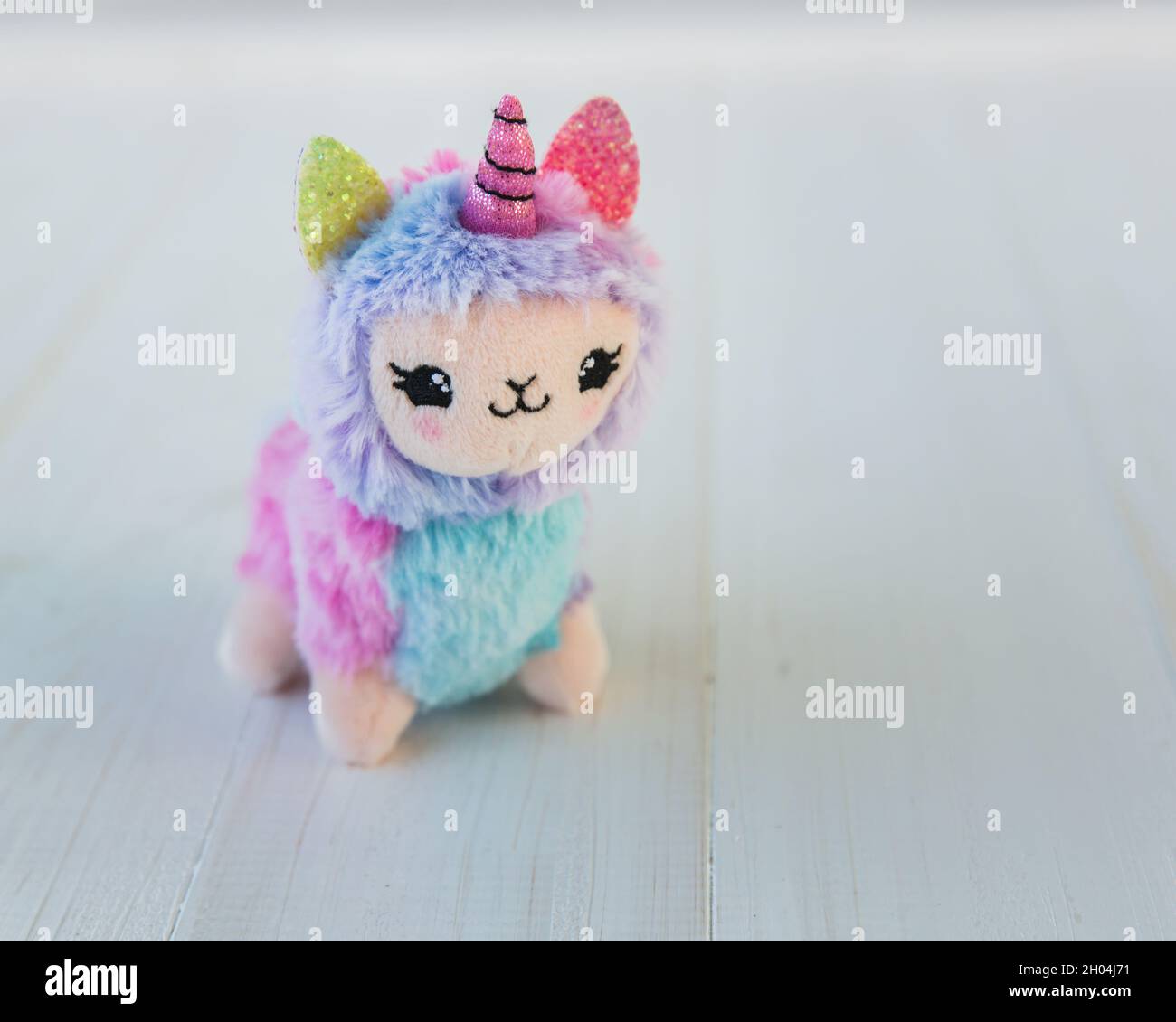 licorne en peluche colorée sur fond de bois blanc.Jouet pour enfants célèbre et populaire. Banque D'Images