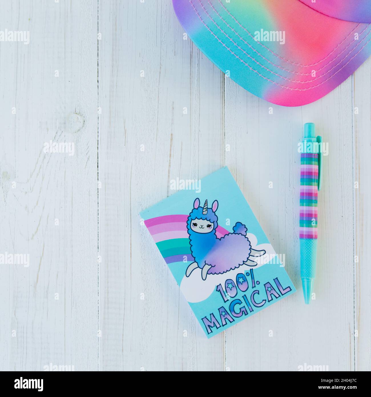 Carnet avec licorne lama et arc-en-ciel avec stylo en gel coloré et casquette arc-en-ciel sur fond blanc en bois.Idée de table de bureau Girly.Retour à l'école con Banque D'Images