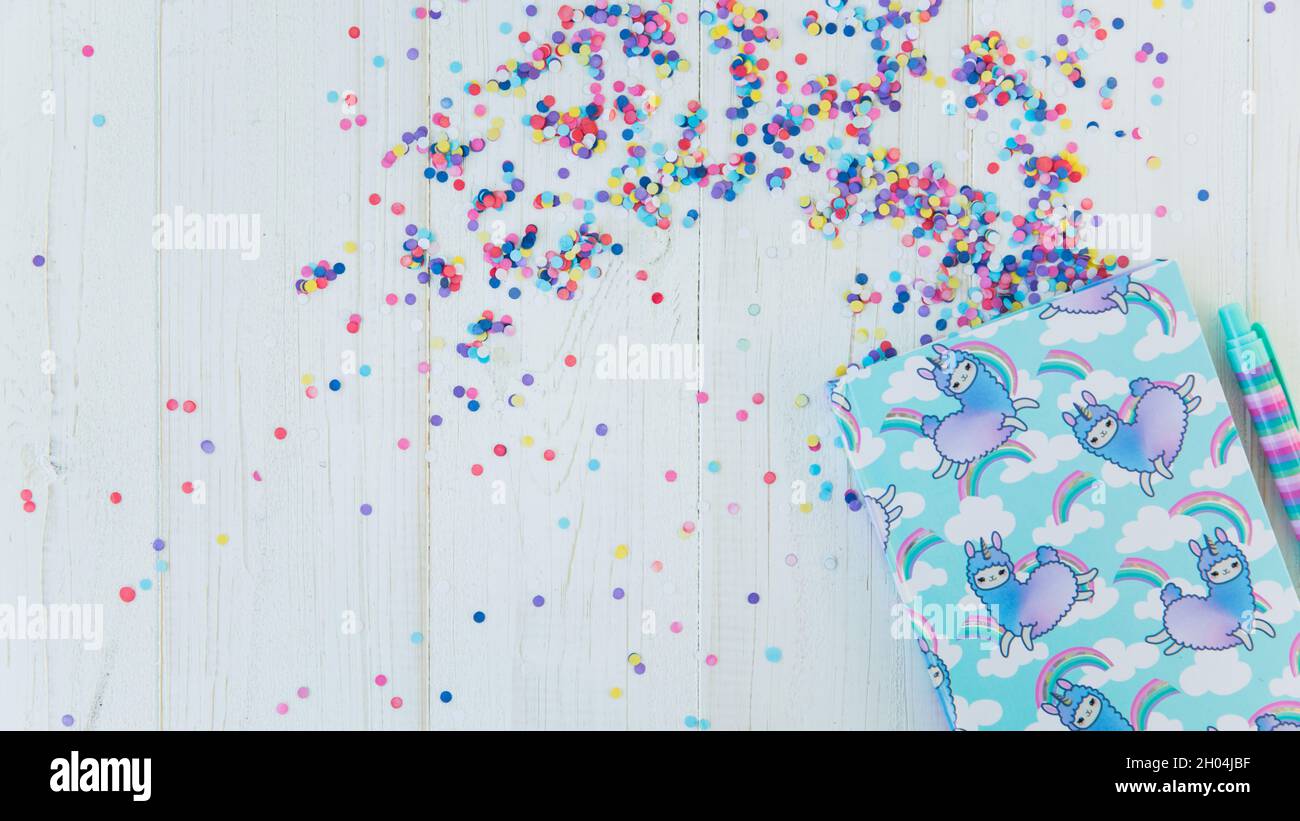 Cahier avec licorne lama et arc-en-ciel avec stylo de gel coloré sur fond blanc en bois avec confetti.Idée de table de bureau Girly.Retour à l'école conce Banque D'Images