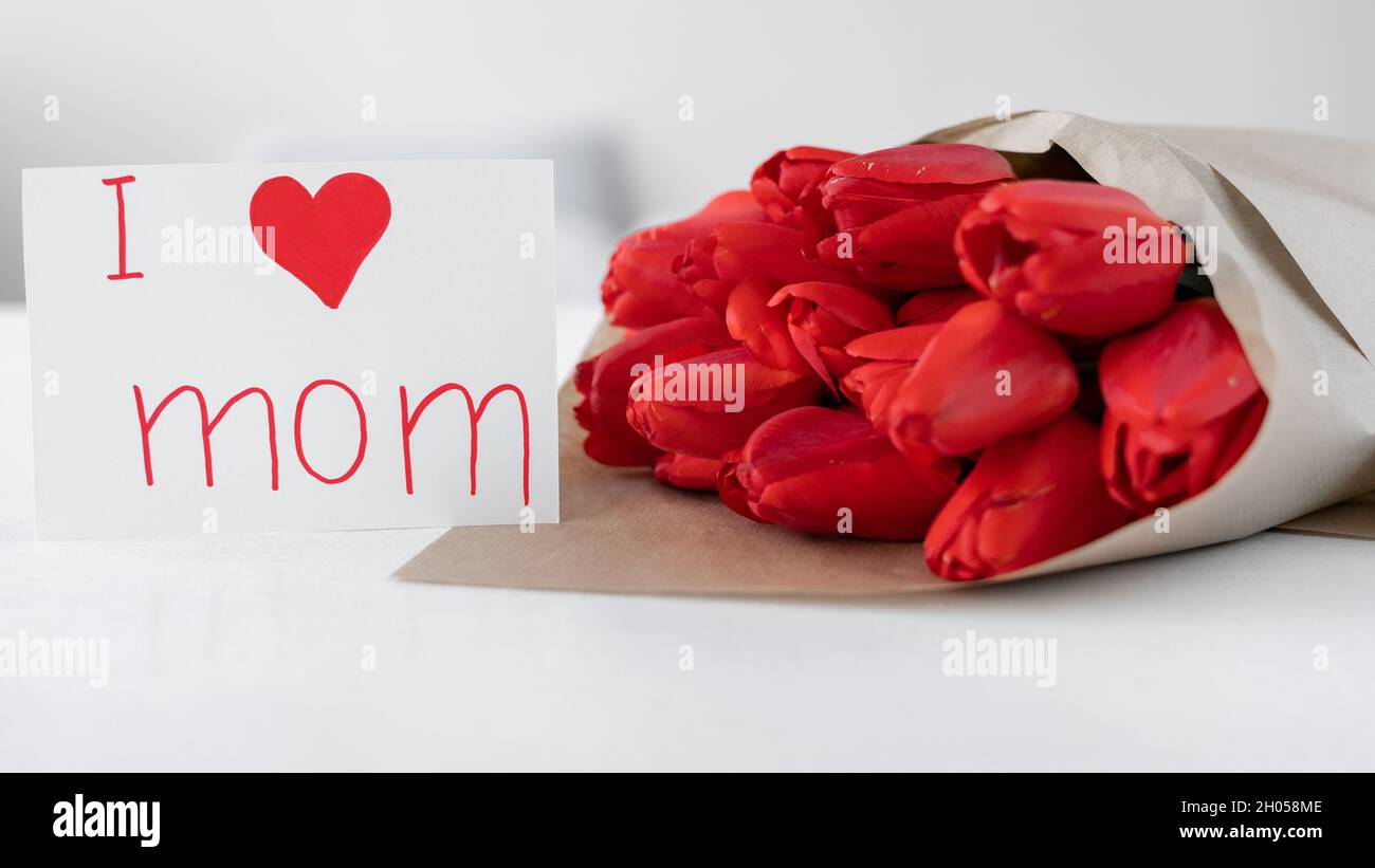 Fête des mères.Un bouquet de tulipes rouges et une carte avec l'inscription J'aime maman sur fond blanc.Fleurs en papier artisanal.Vacances de maman fleur. Banque D'Images