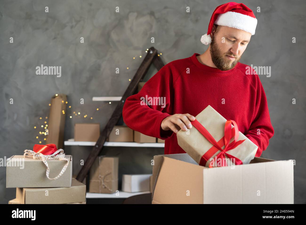 Un propriétaire de petite entreprise dans un chapeau de père Noël collecte  des cadeaux dans un sac.Achats en ligne et vendeur de magasin.Un homme  prépare une commande avec un cadeau pour Noël