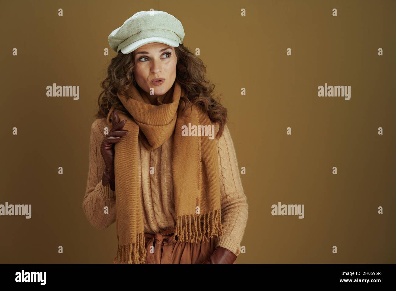 Bonjour automne. Surprise femme de 40 ans en foulard avec des gants en cuir regardant l'espace de copie sur fond beige. Banque D'Images