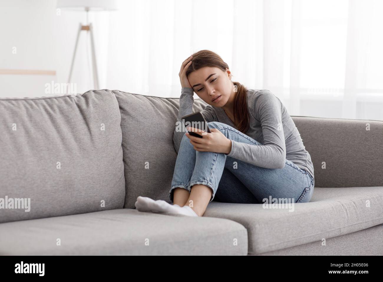 Triste déprimé inquiète femme européenne millénaire assise sur un canapé recevant de mauvaises nouvelles, en attente d'appel ou de réponse d'un gars à l'intérieur de la maison.Problèmes à Banque D'Images