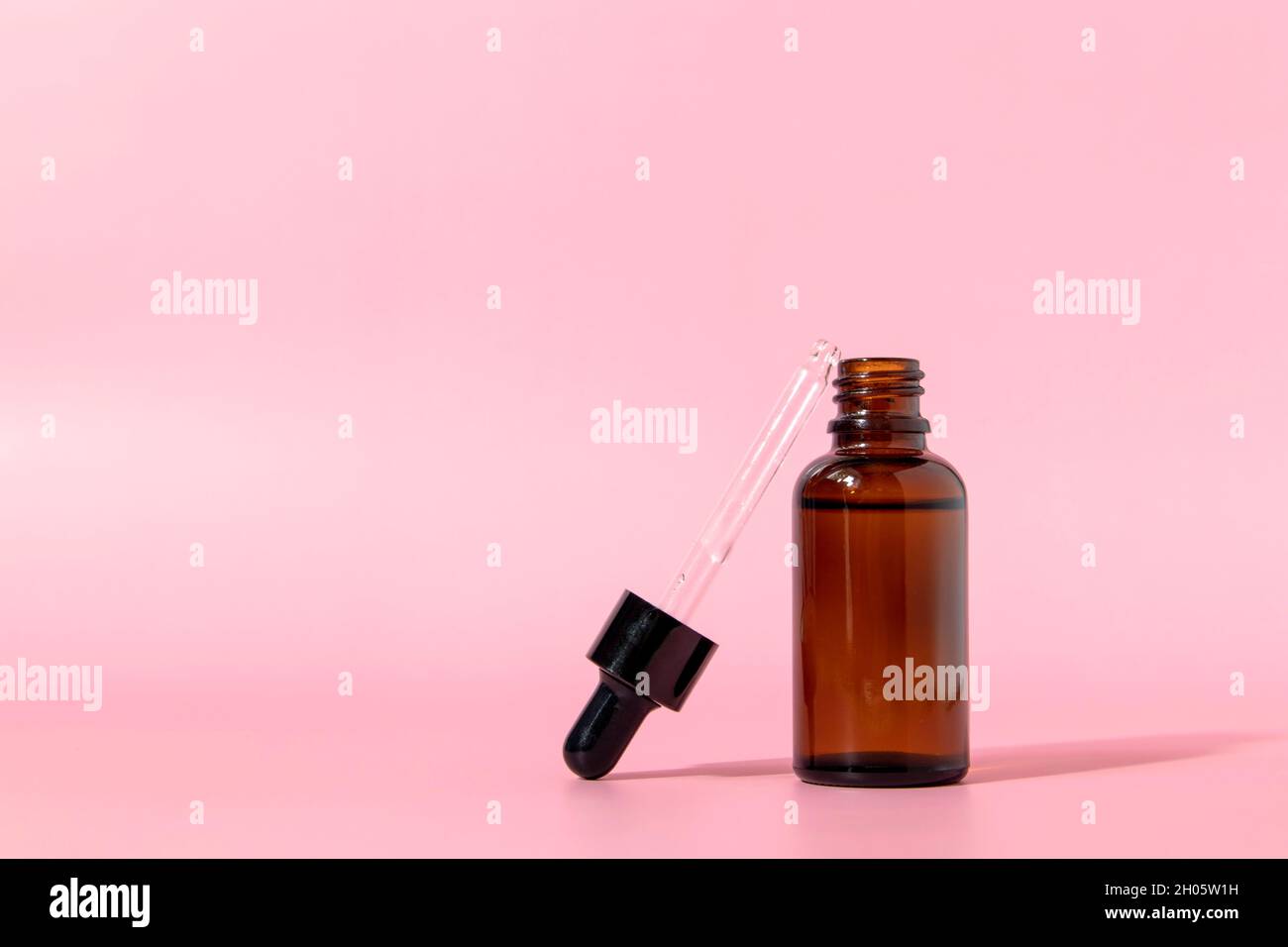 Flacon en verre brun avec compte-gouttes sur fond rose. Emballage de sérum ou d'huile essentielle. Maquette d'un produit cosmétique. Vue de face avec espace de copie. Banque D'Images