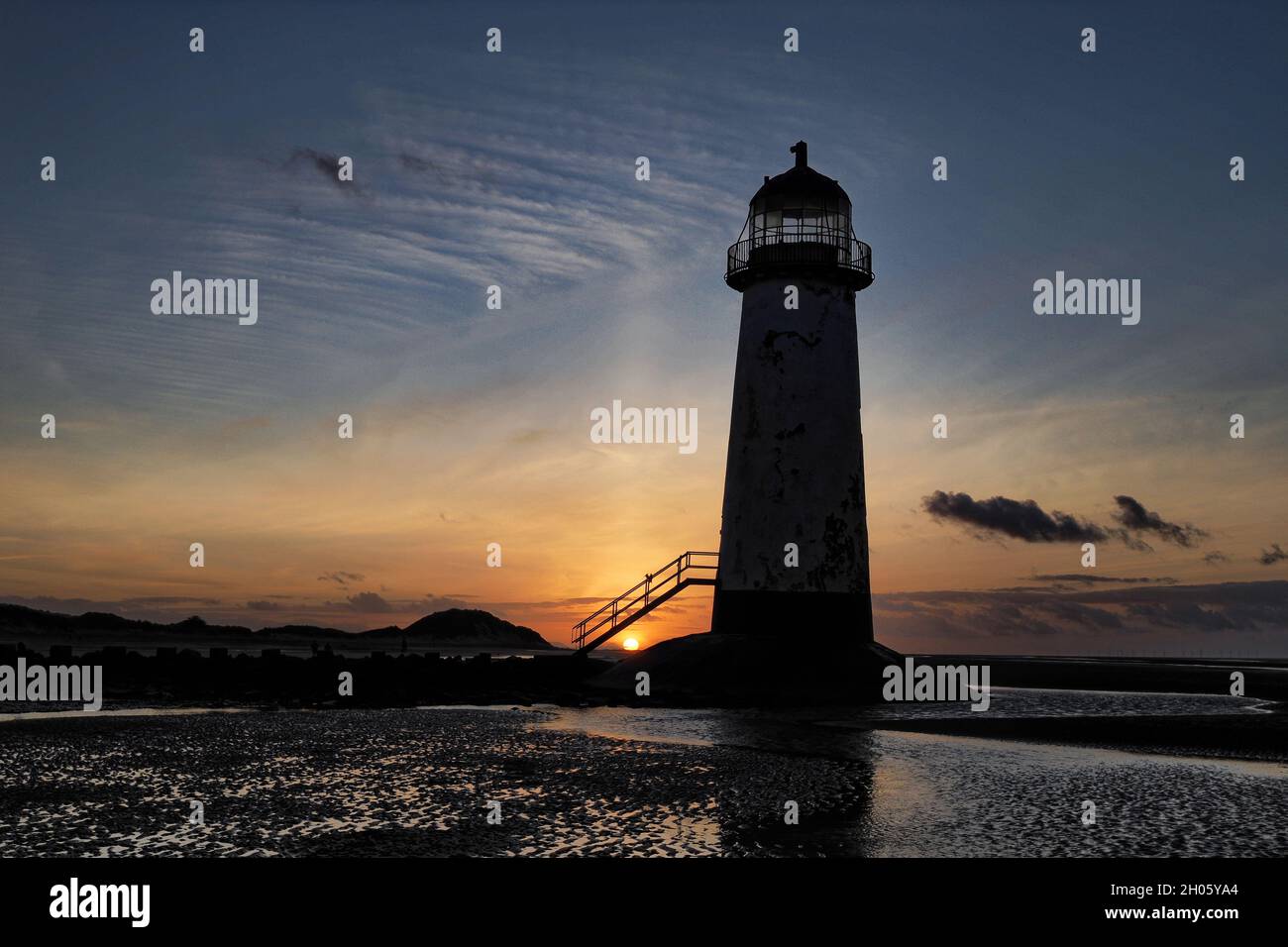 Le soleil se couche derrière les dunes contre le phare de point of Ayr à Talacre, au nord du pays de Galles. Banque D'Images