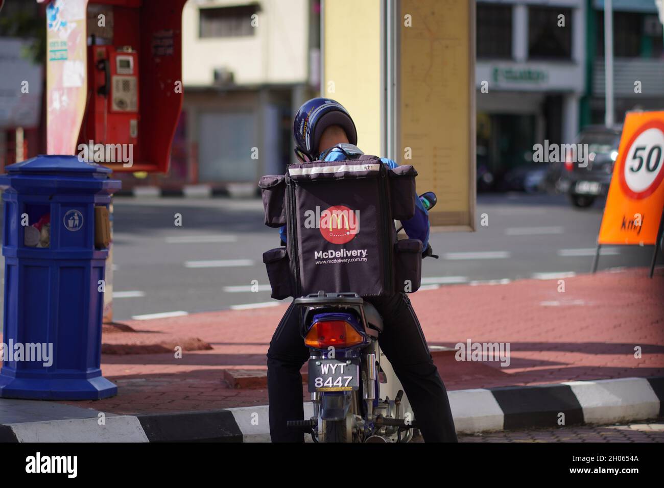 Un pilote de livraison McDonald's attendant sur une moto sur le côté de la route de la ville. Banque D'Images