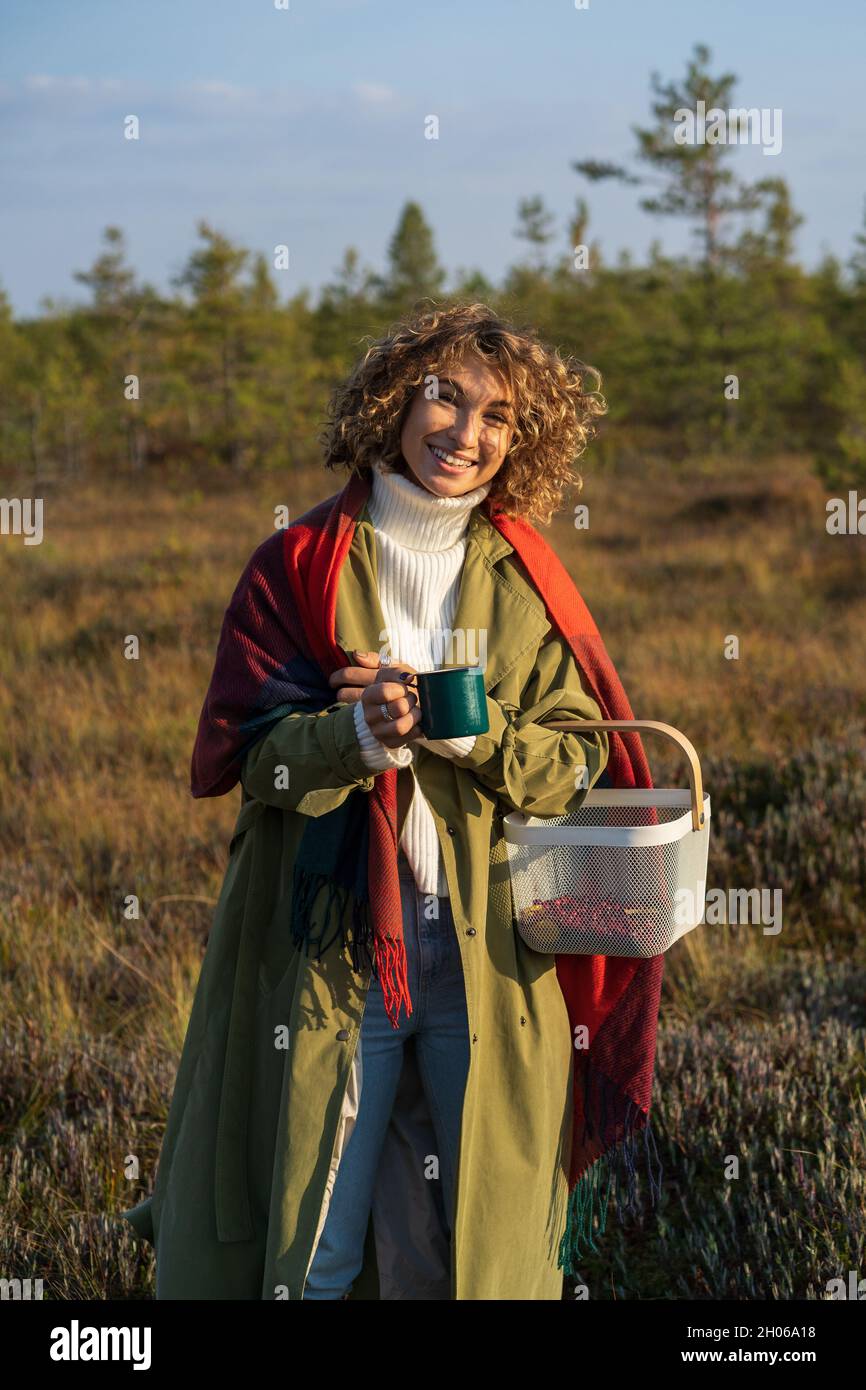 Bonne femme Profitez de la chaude journée d'automne, du temps ensoleillé dans la campagne, en tenant une tasse de thé chaud et souriant Banque D'Images