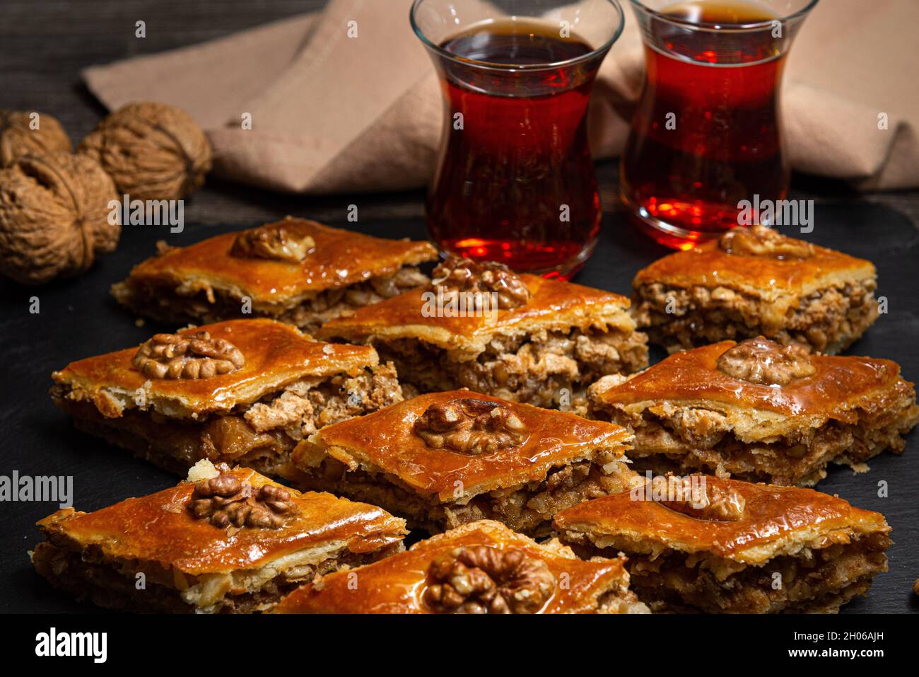 Baklava au miel et noix sur ardoise noire.Portions de sucreries orientales.Morceaux sucrés turcs.Thé versé dans le verre armudu à l'arrière-plan. Banque D'Images