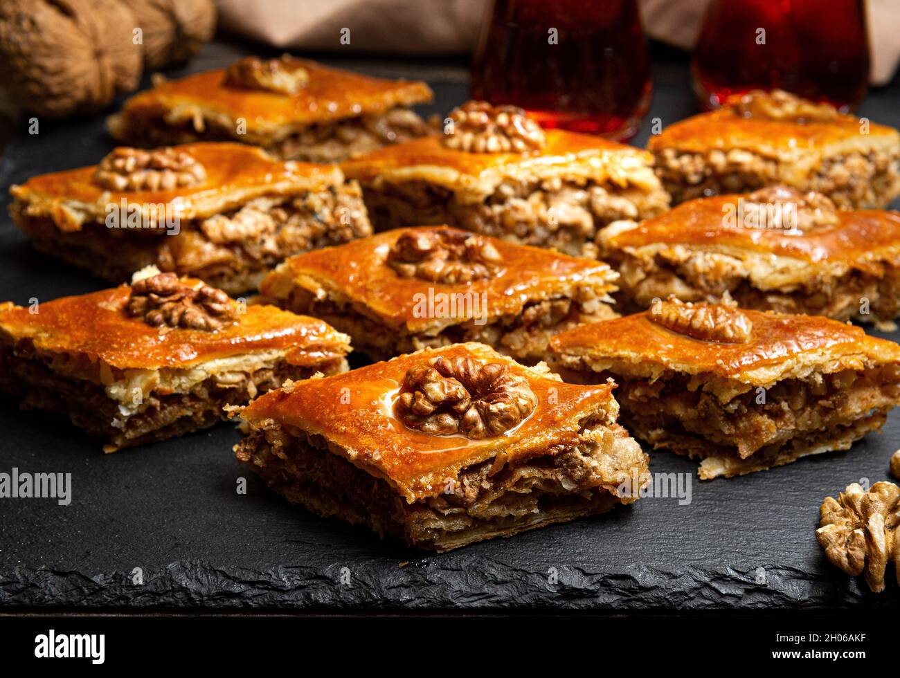 Baklava au miel et noix sur ardoise noire.Portions de sucreries orientales.Morceaux sucrés turcs.Thé versé dans le verre armudu à l'arrière-plan. Banque D'Images