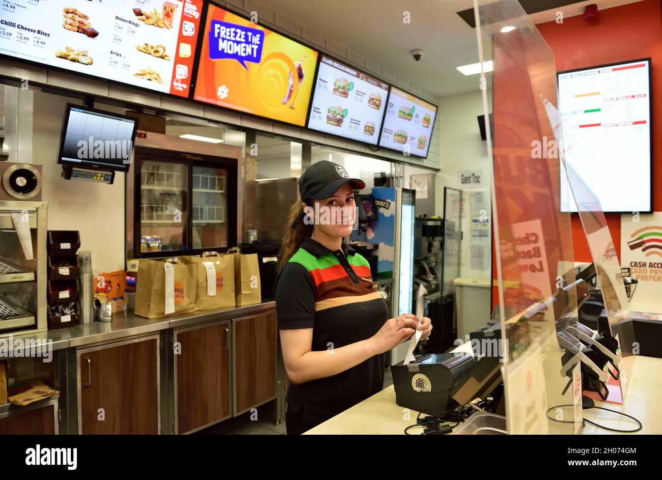 Jeune femme attirante travaillant dans Burger King fast food point derrière Covid-19 Screen, Royaume-Uni Banque D'Images